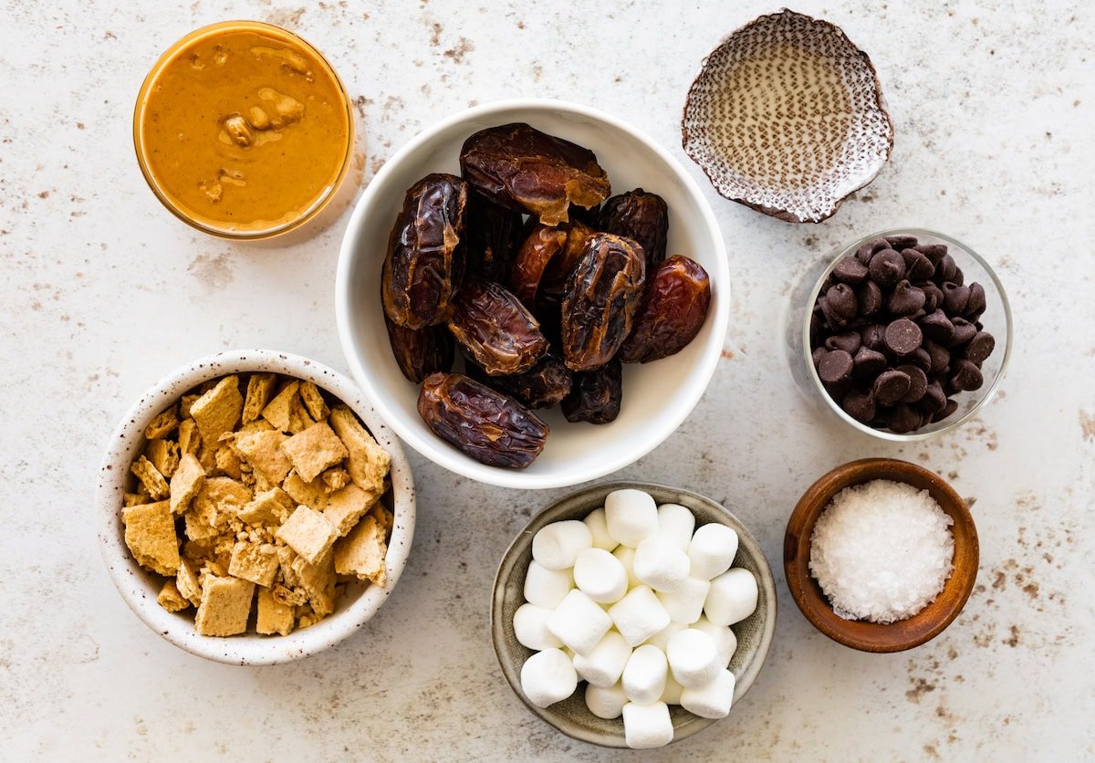 peanut butter, dates, chocolate chips, coconut oil, graham crackers, mini marshmallows, and sea salt in bowls to make s'mores date bark. 