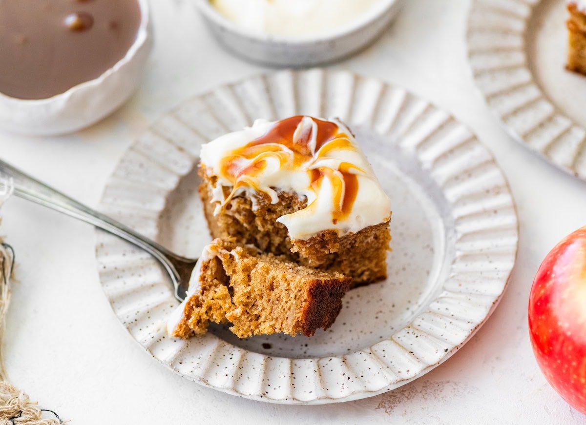 piece of apple spice cake with salted caramel cream cheese frosting on plate with fork. 
