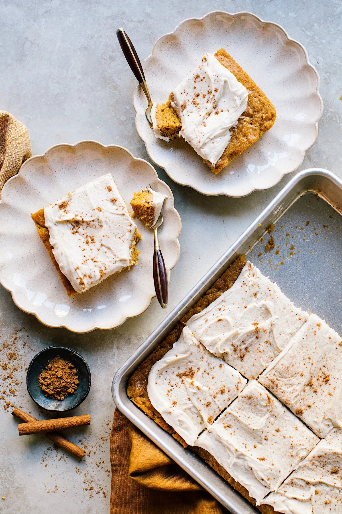 pumpkin sheet cake with brown butter cream cheese frosting in pan and pieces on plates with forks.