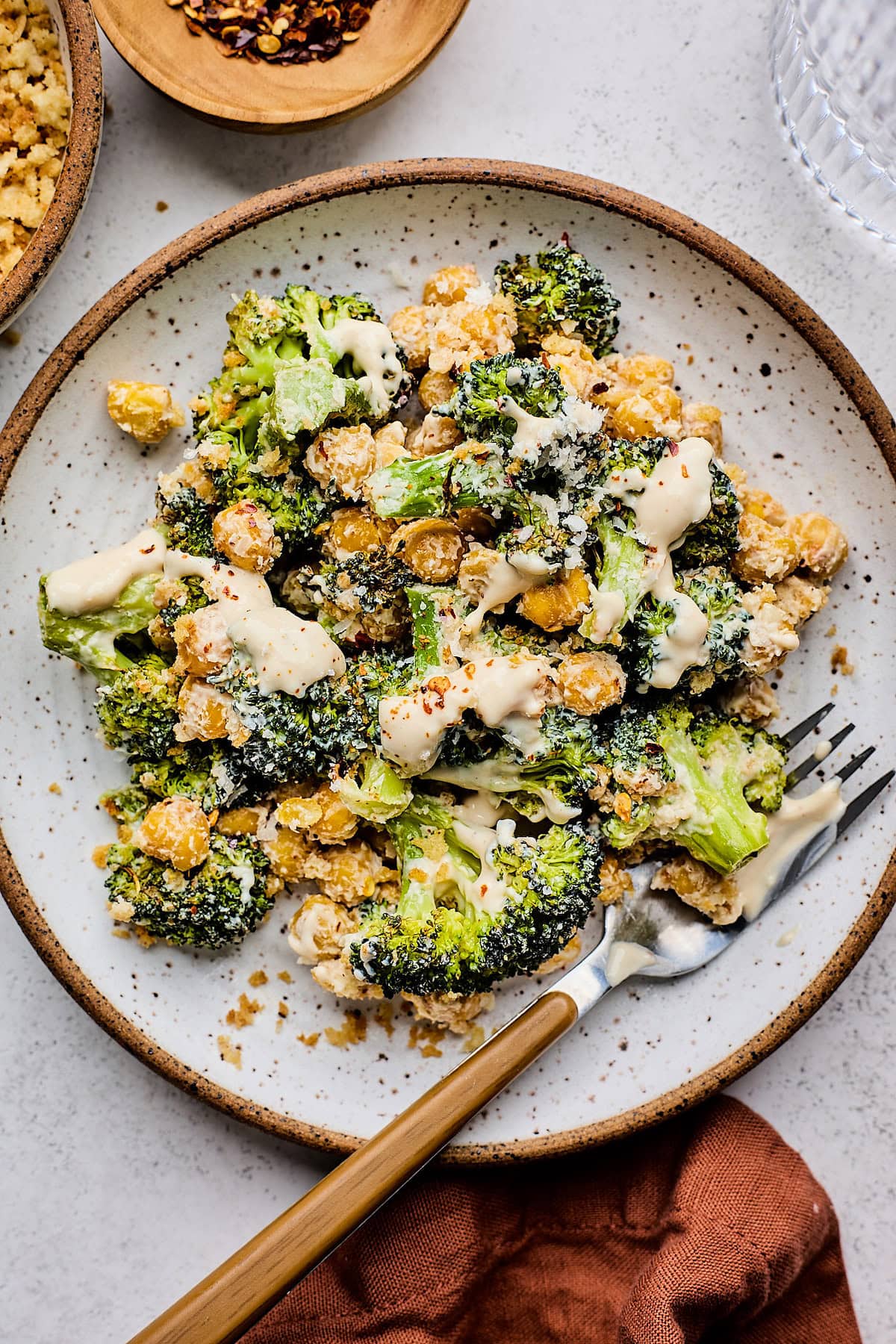 broccoli Caesar salad with chickpeas and toasted breadcrumbs drizzled with dressing on plate with fork.