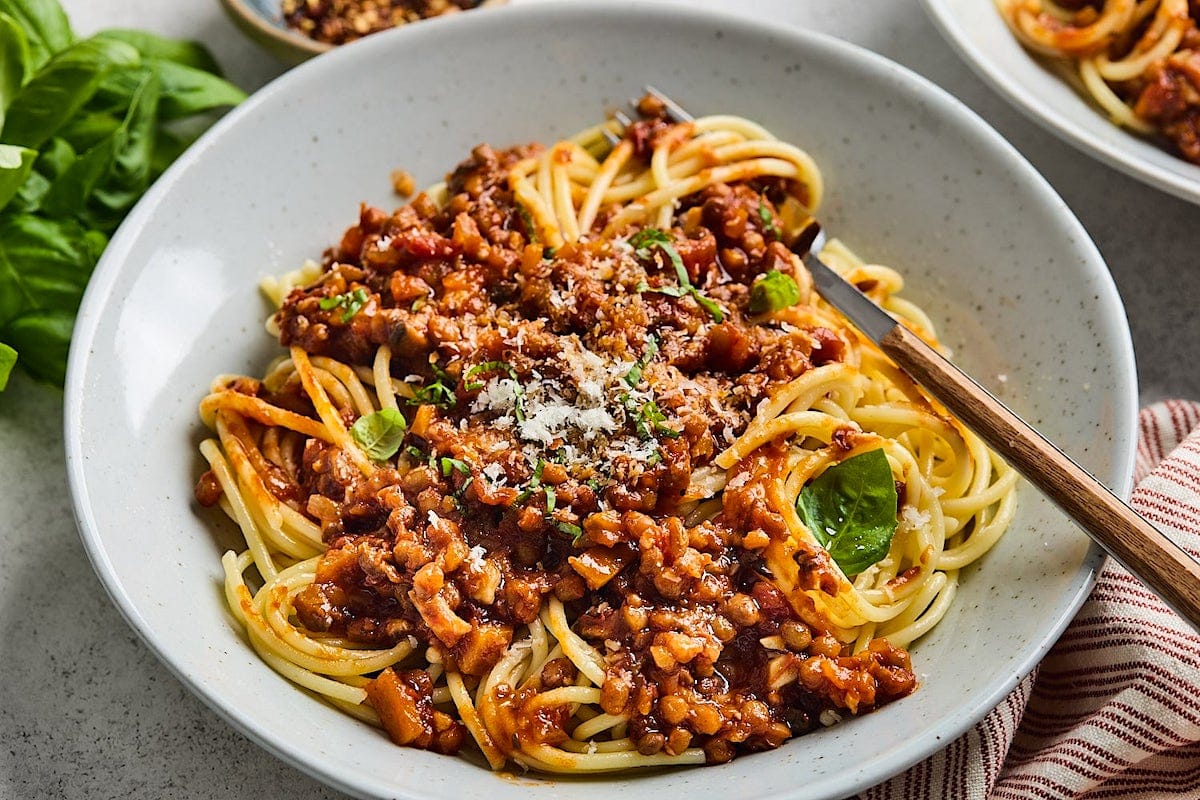 lentil bolognese over pasta with parmesan cheese in bowl with fork. 