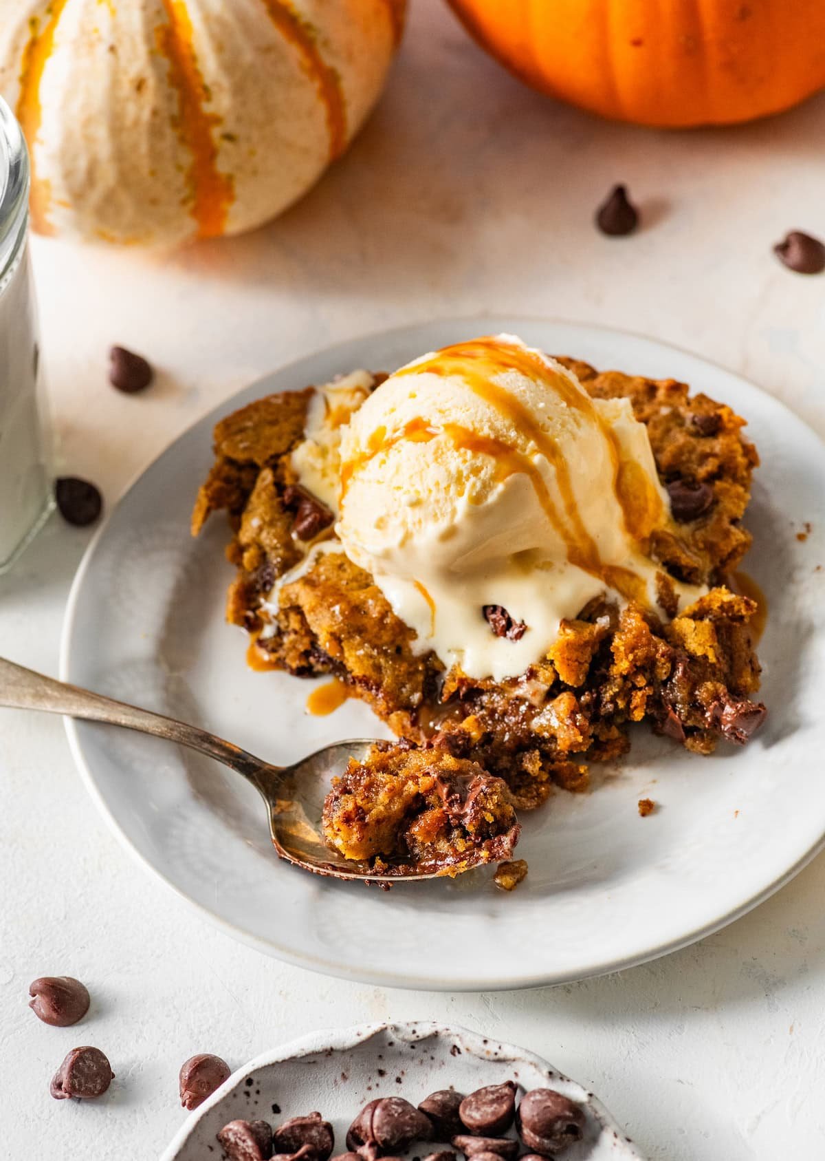 piece of pumpkin chocolate chip skillet cookie on plate with vanilla ice cream and salted caramel sauce and spoon. 