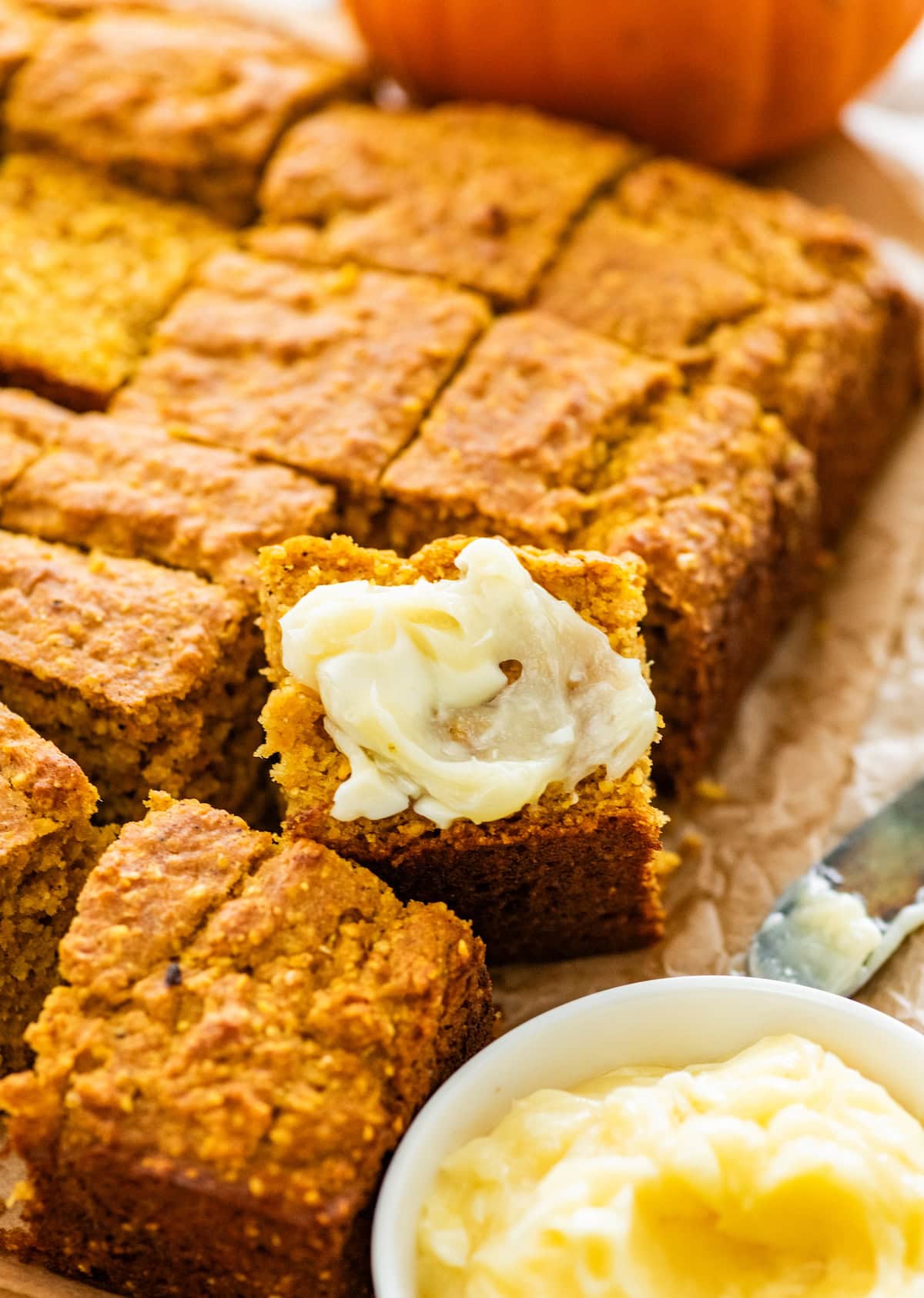 pumpkin cornbread cut into squares with one piece topped with butter.