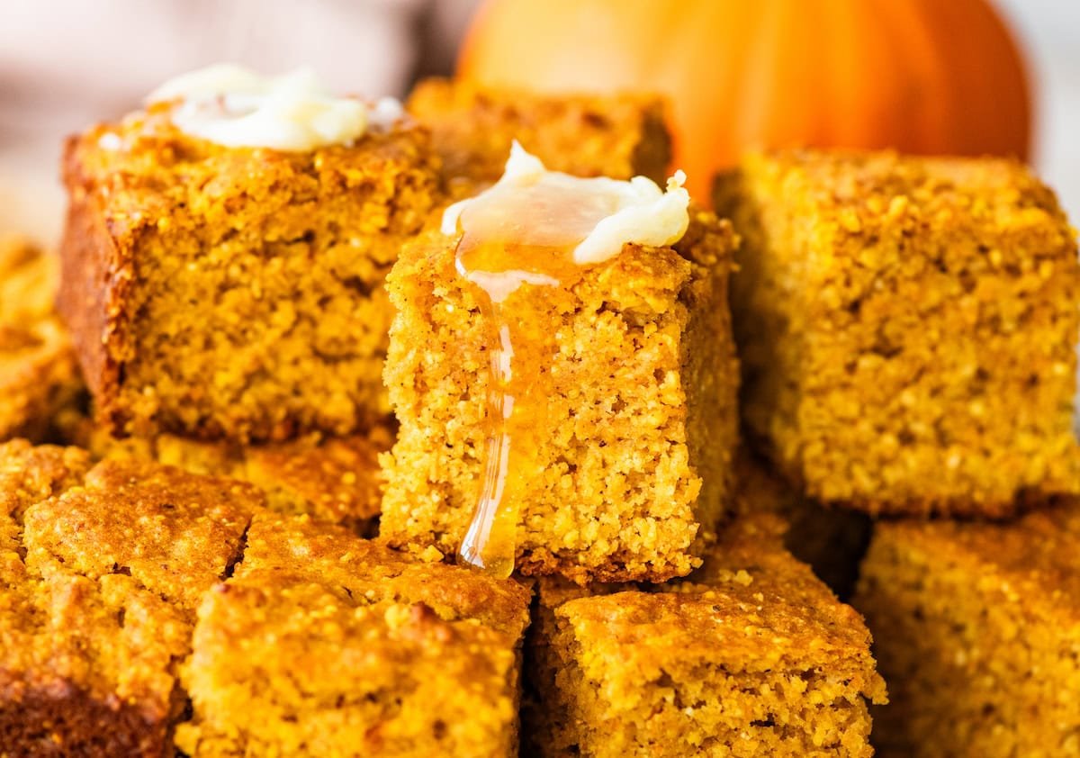 pumpkin cornbread squares stacked with butter and honey.