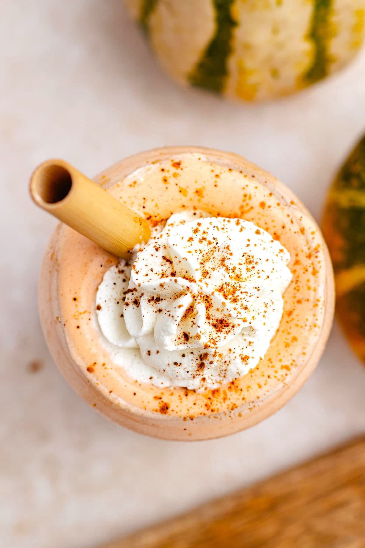 close up of pumpkin smoothie topped with whipped cream and a sprinkle of cinnamon and straw.