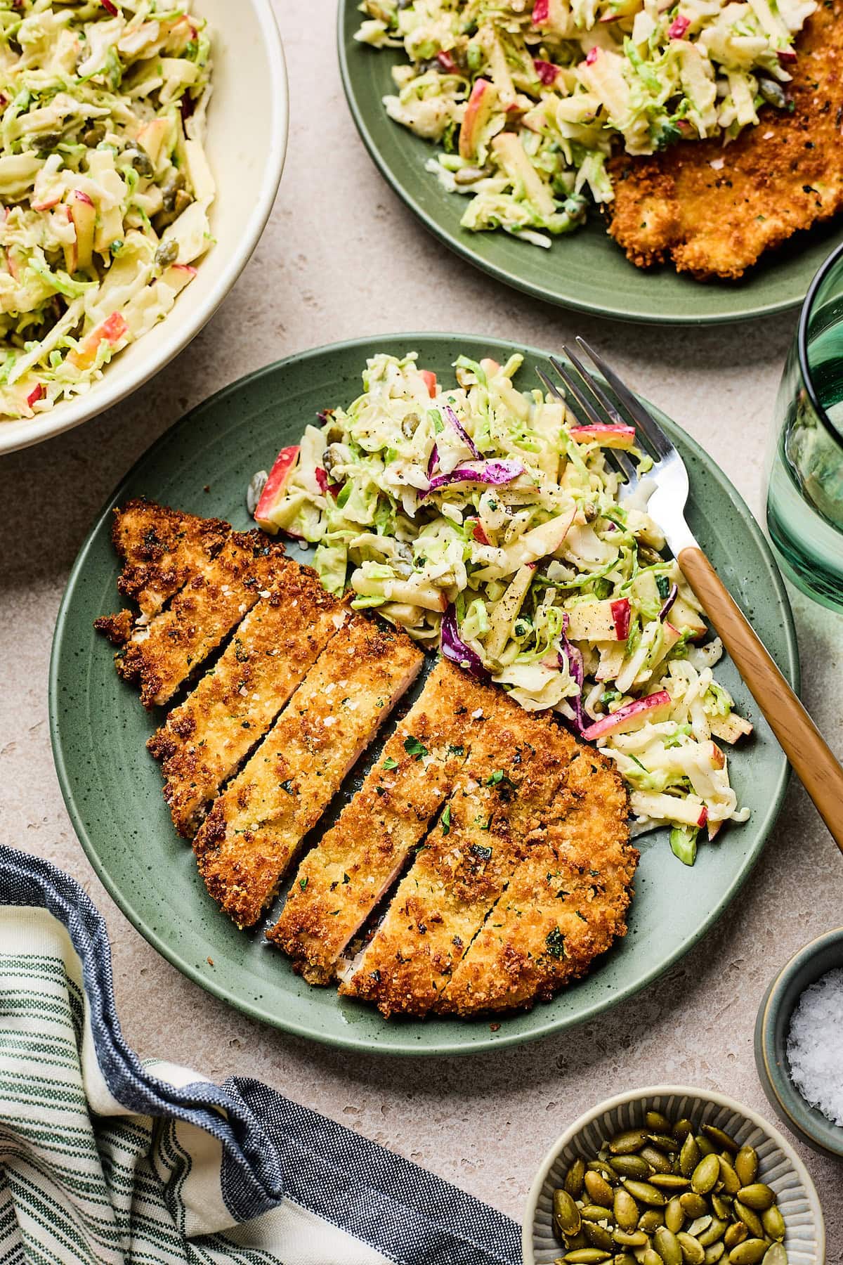 crispy chicken cutlet cut into pieces on plate with apple slaw and fork.