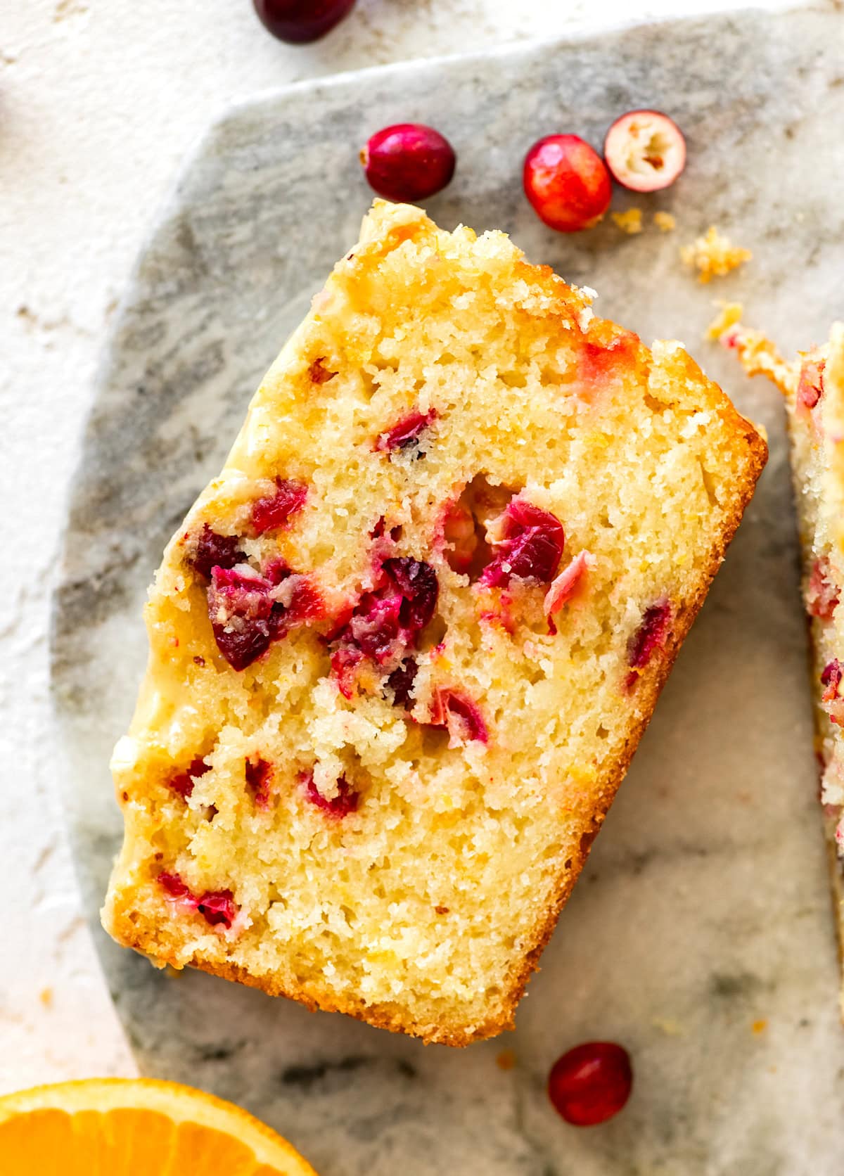 piece of cranberry orange bread with orange glaze on marble board. 
