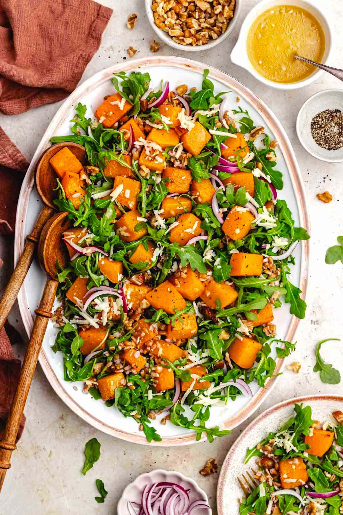 roasted butternut squash salad with farro, red onion, white cheddar, and walnuts on platter with wood salad servers.