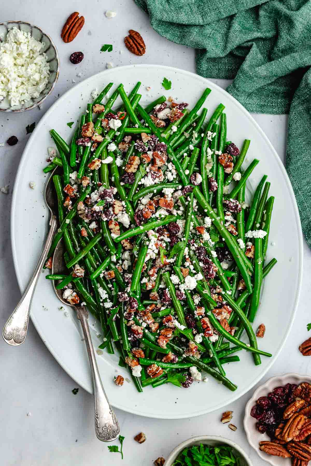 fresh green beans with pecan cranberry feta crumble on white platter with serving spoons.