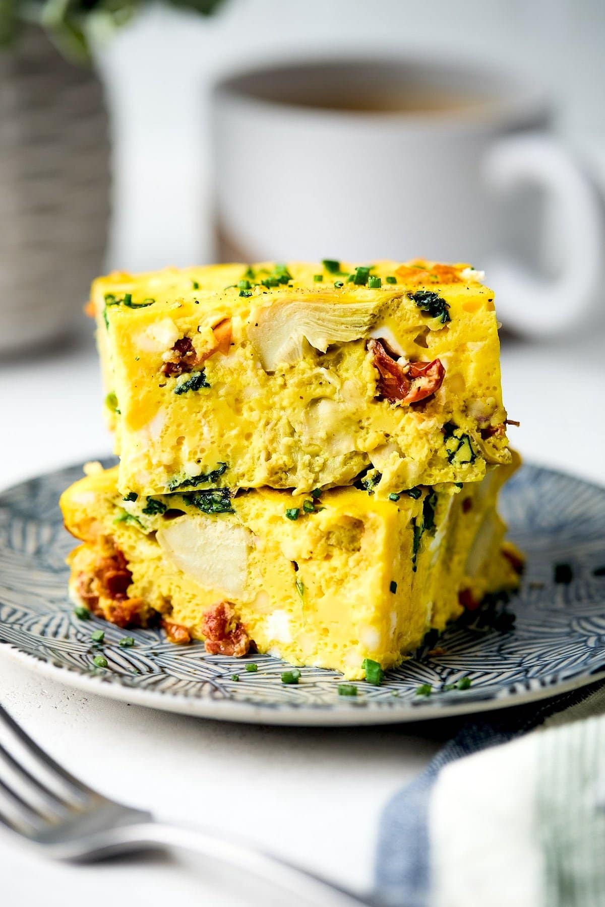 two pieces of Spinach Artichoke Sun-Dried Tomato Breakfast Casserole stacked on plate.