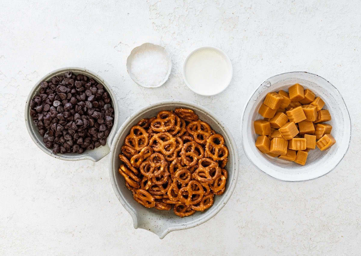 chocolate chips, pretzels, caramels, heavy cream, and flaky sea salt in bowls to make pretzel bark.