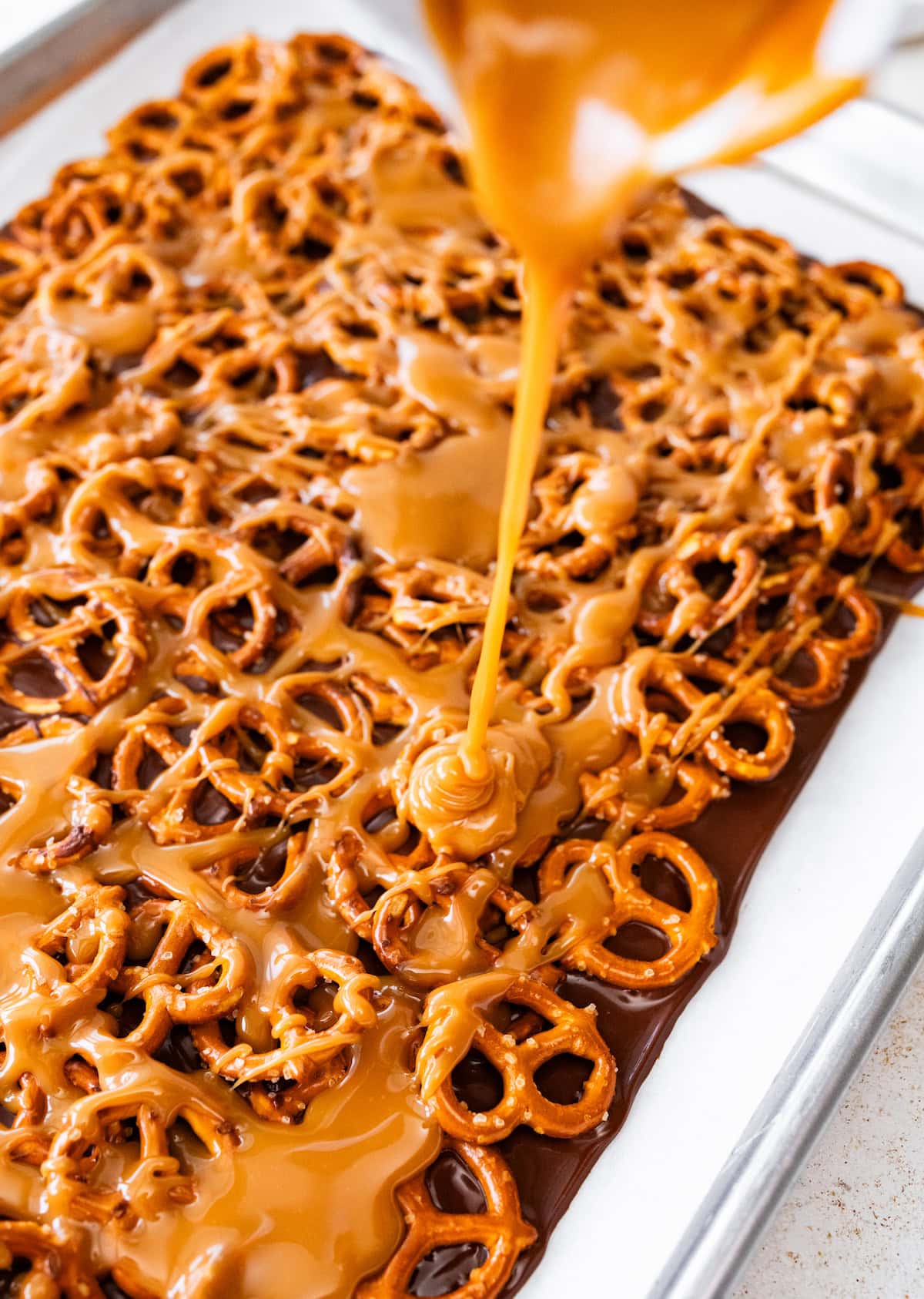 caramel being poured over chocolate pretzel bark.