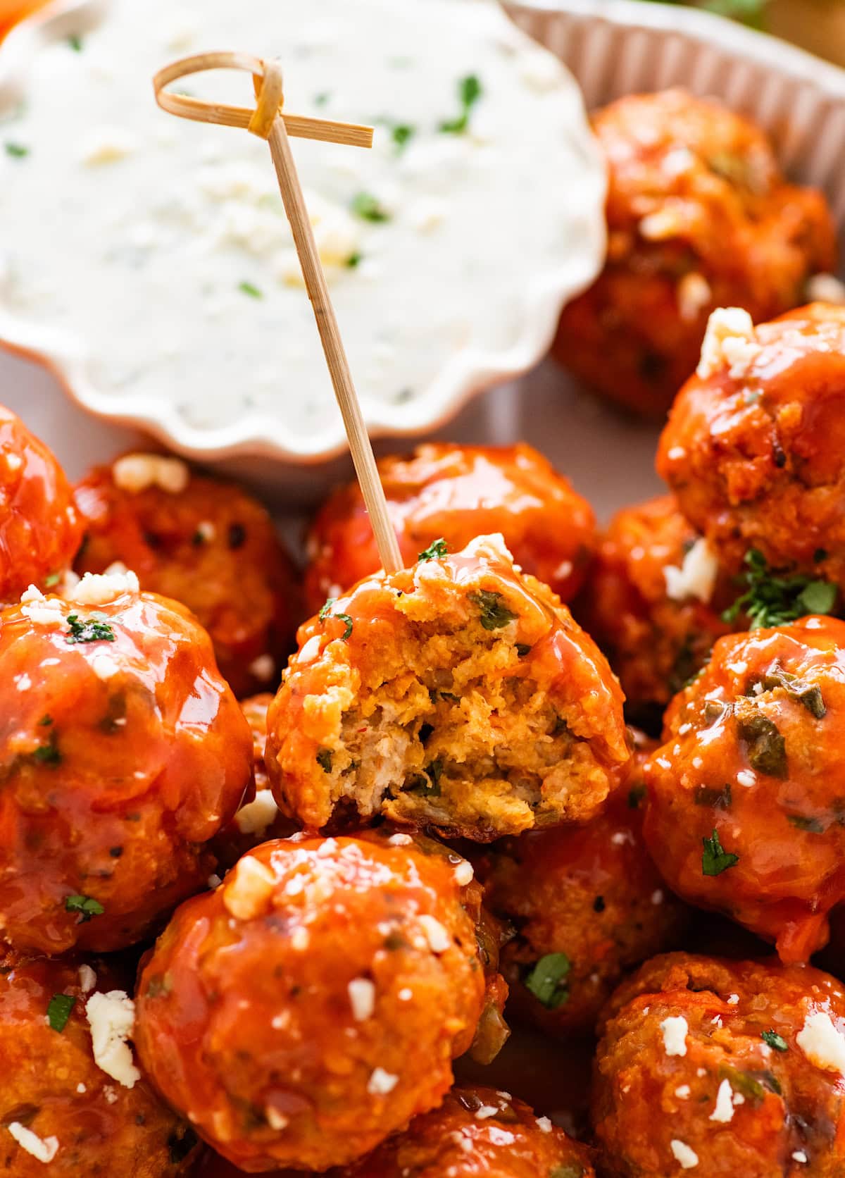 close up of buffalo chicken meatball on toothpick with bite missing and blue cheese dip.