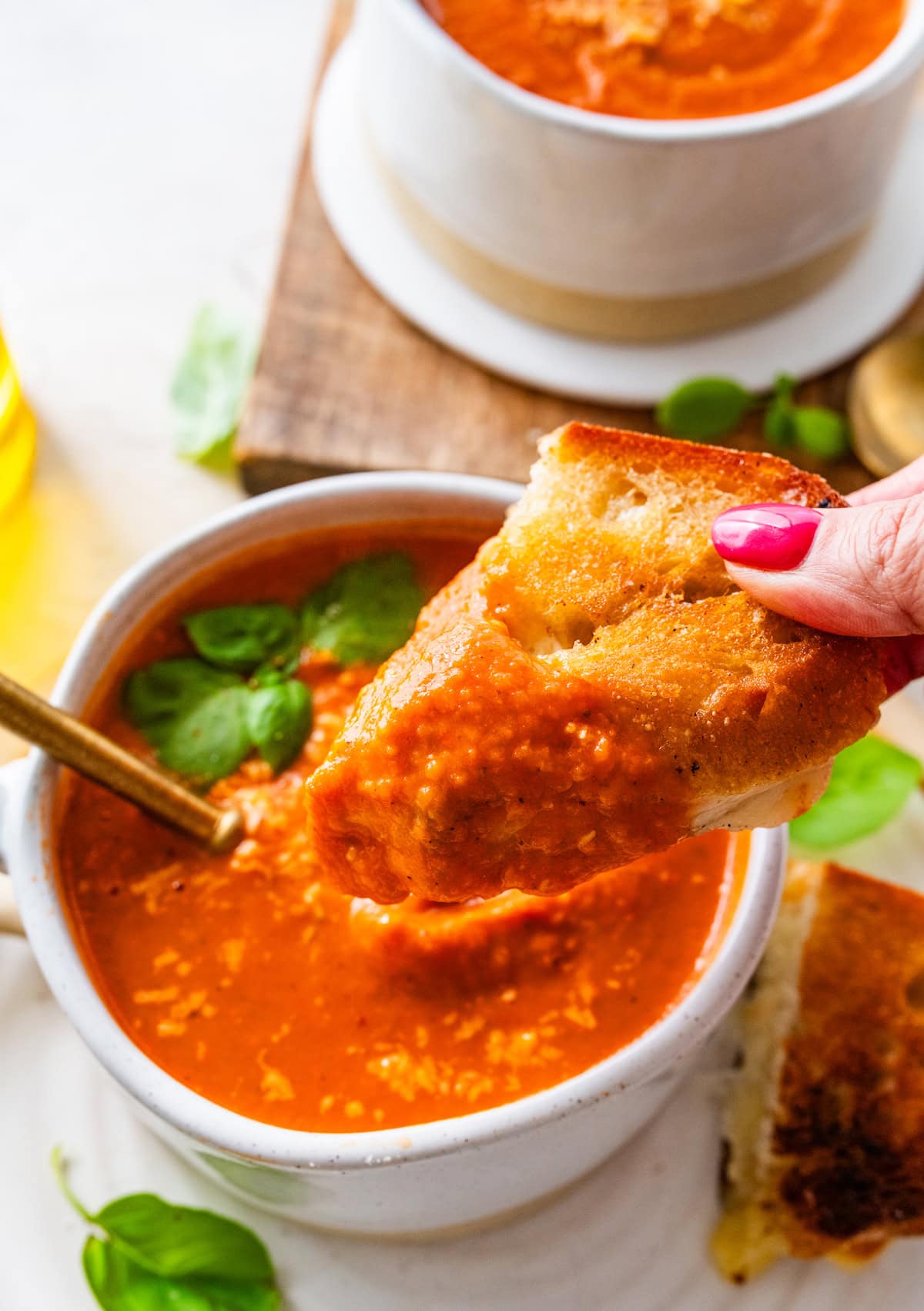 grilled cheese being dunked into a bowl of creamy tomato basil soup.