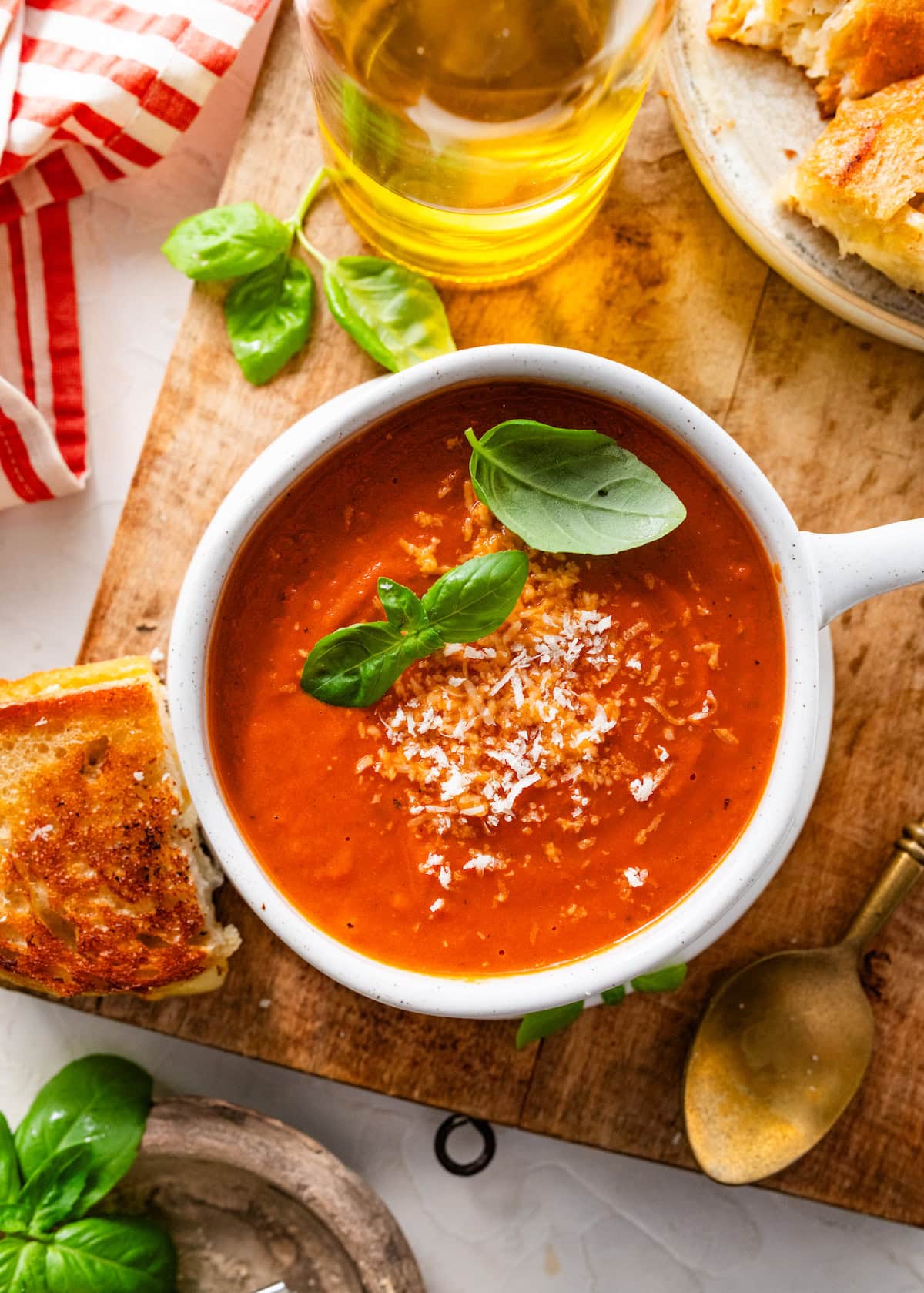 creamy tomato basil soup in bowl with parmesan cheese and fresh basil on wood board with grilled cheese.