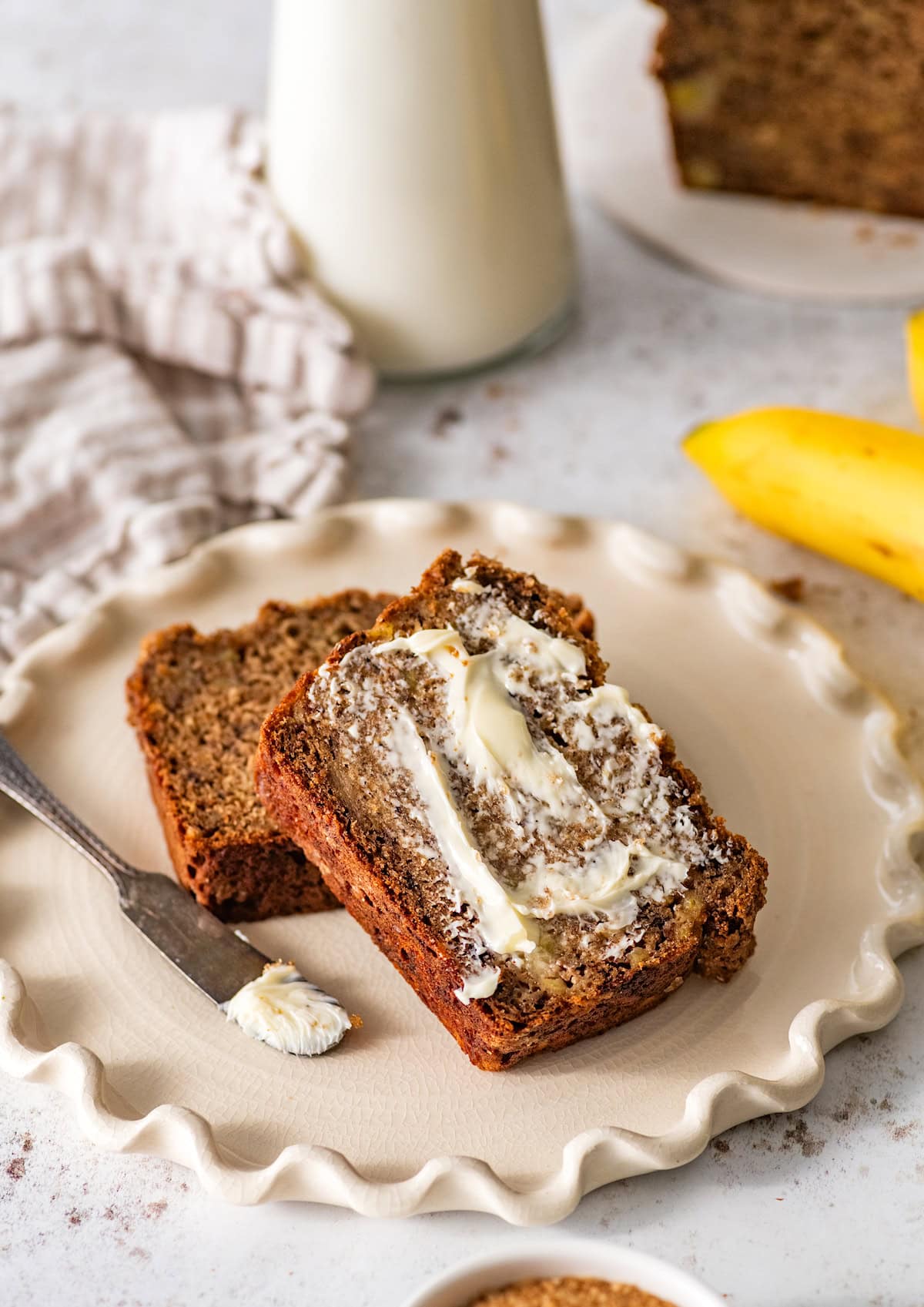 healthy banana bread slices on plate with butter and spreading knife.