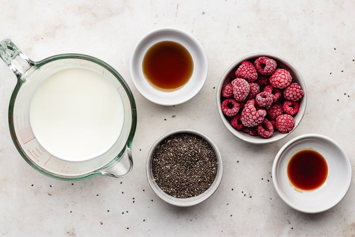 milk, chia seeds, raspberries, maple syrup, and vanilla in bowls to make raspberry chia pudding.