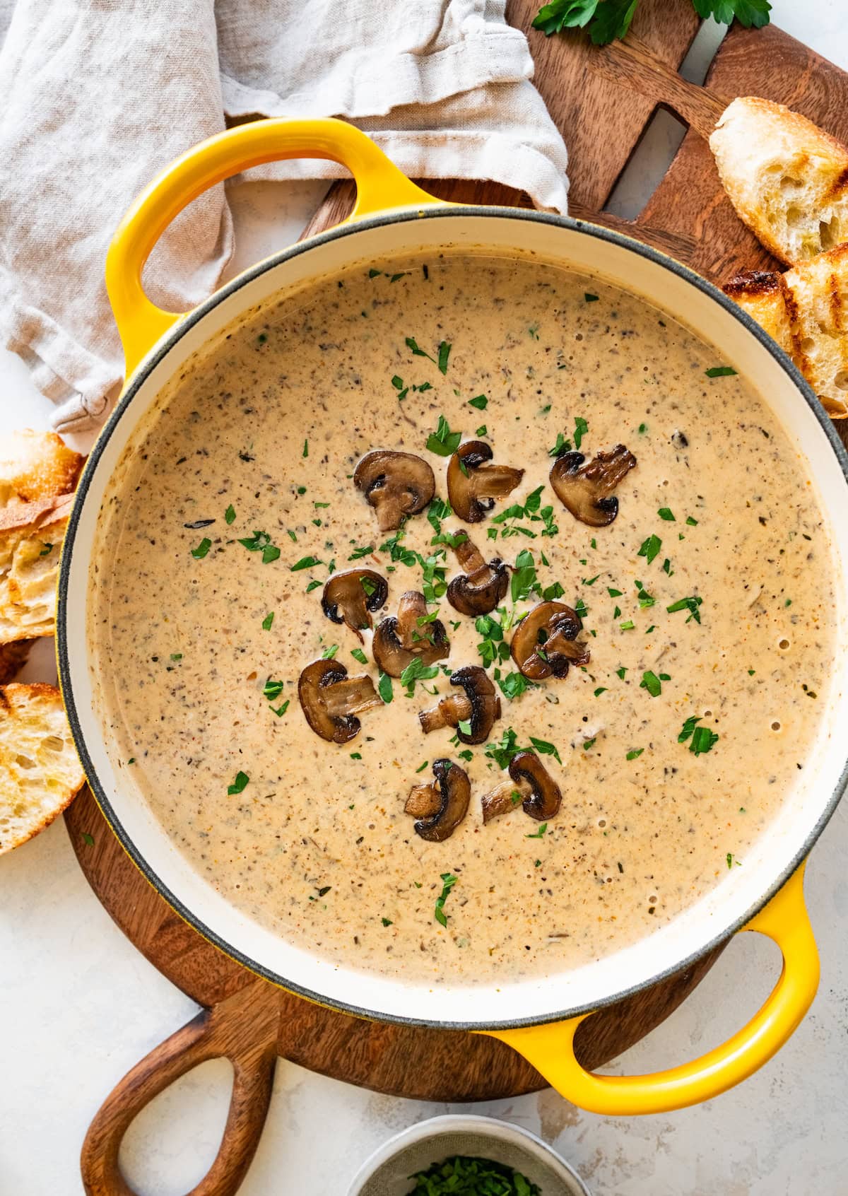 creamy mushroom soup in large pot with fresh mushrooms and parsley on top.