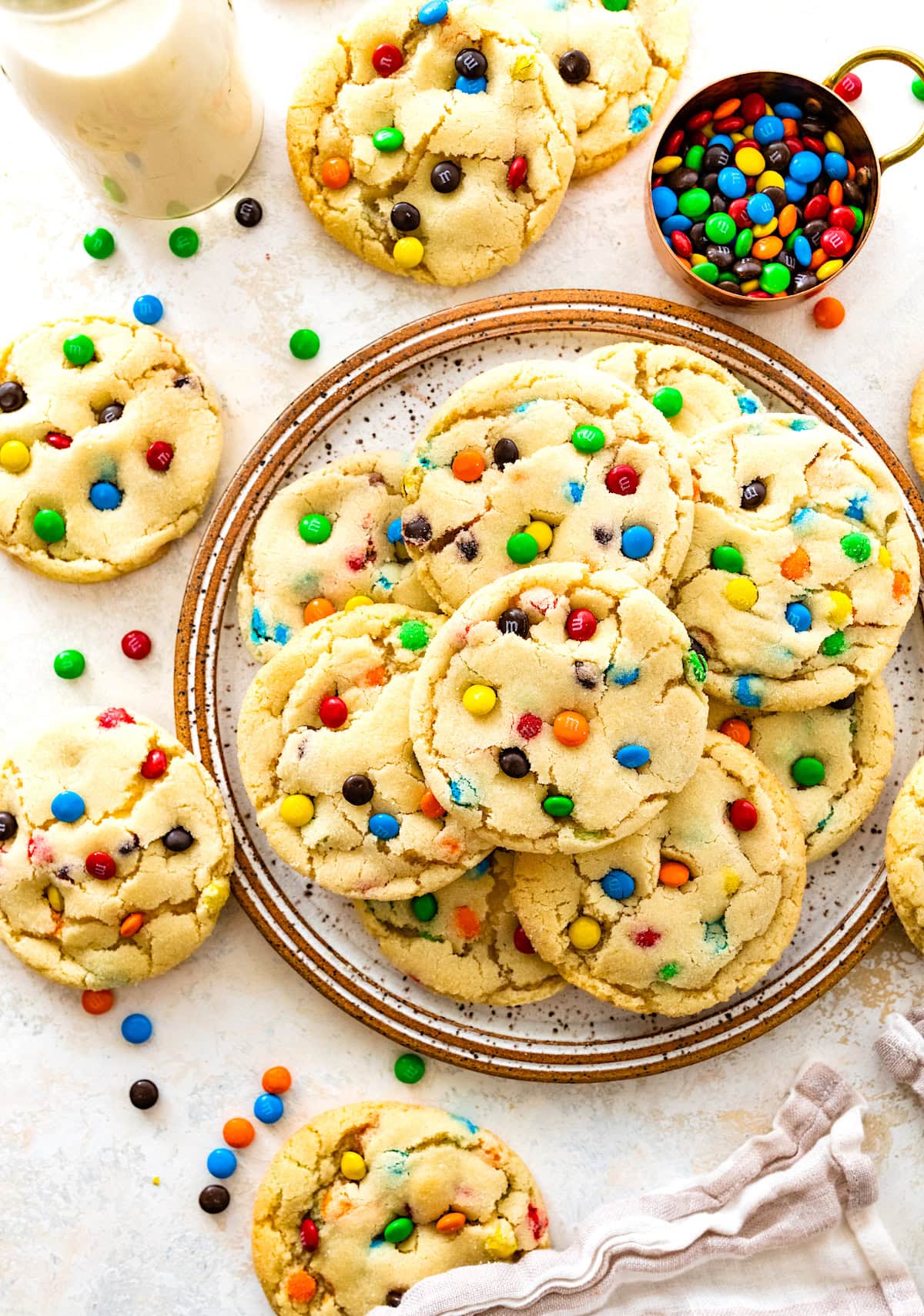 M&M sugar cookies on plate with glass of milk and M&M candies in measuring cup.