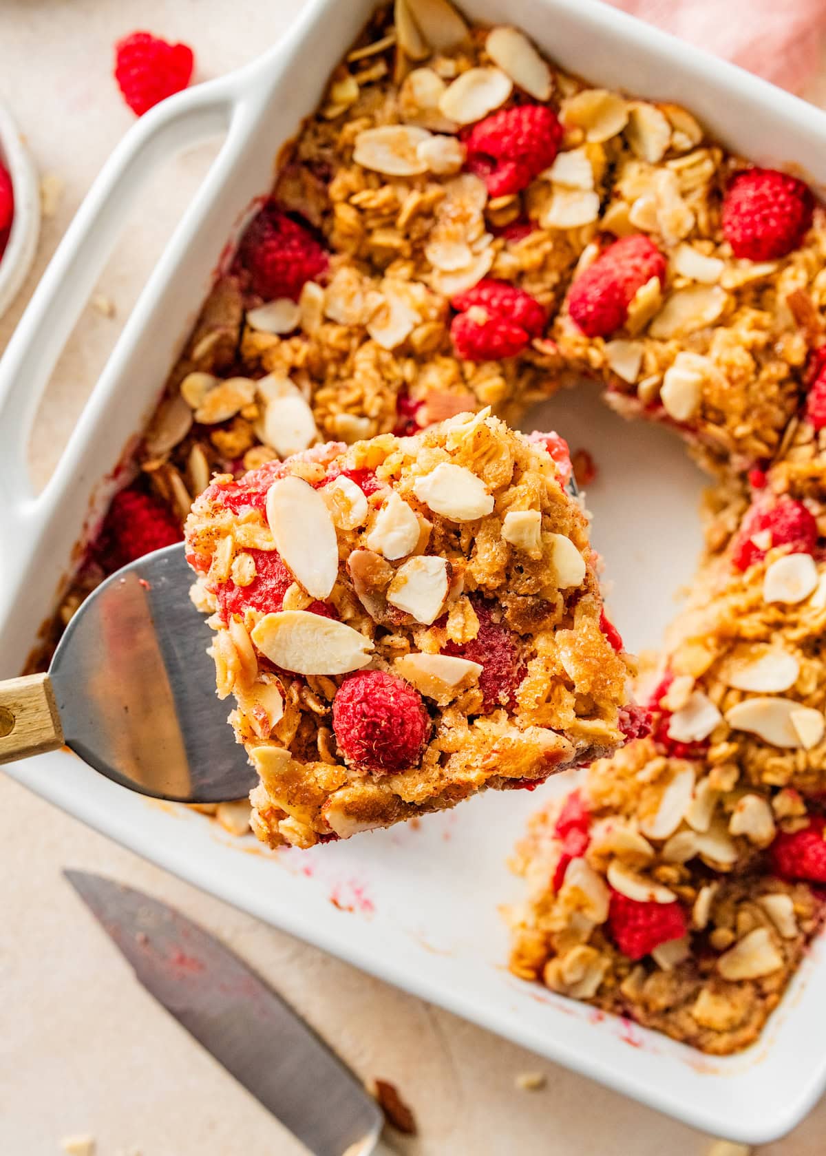 square of raspberry baked oatmeal being lifted out of the pan with a spatula.