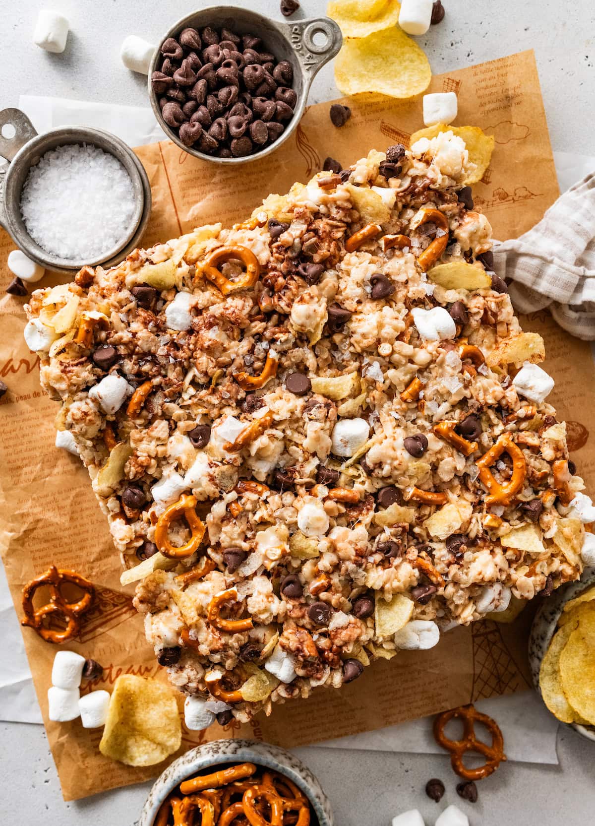 sweet and salty rice krispie treats with potato chips, pretzels, chocolate chips and marshmallows on parchment paper.