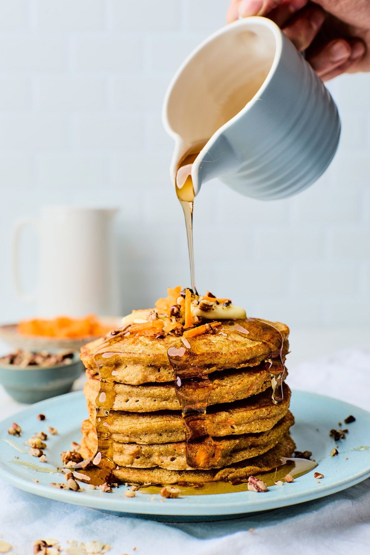 stack of carrot cake pancakes on plate with maple syrup being poured over the top.