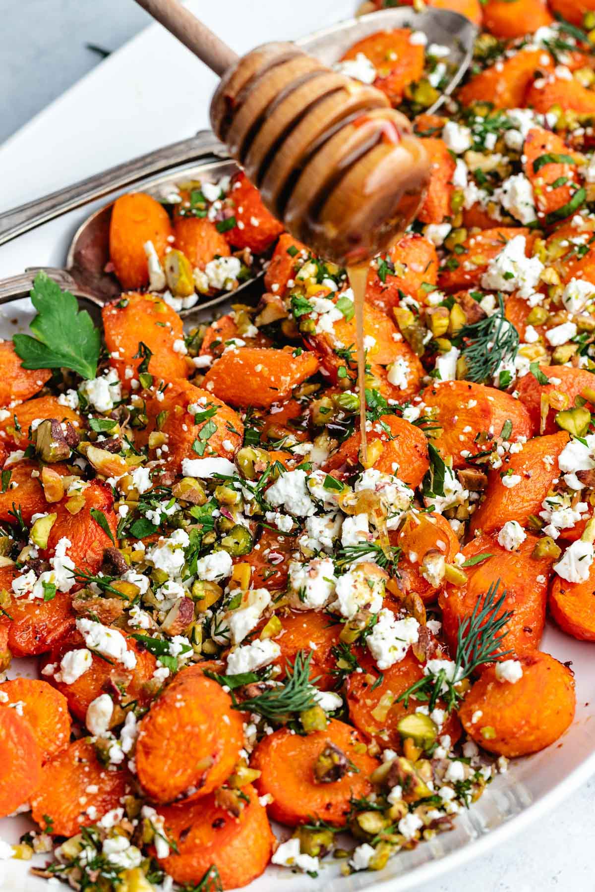 hot honey being drizzled over roasted carrots with pistachios, feta, and herbs.