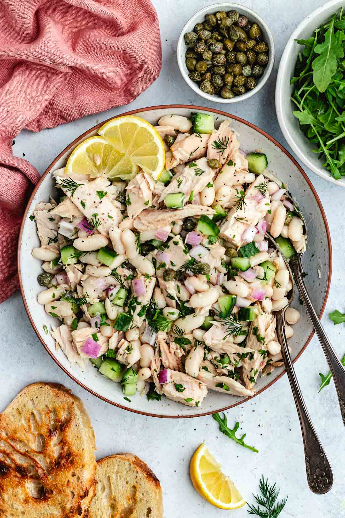 Tuna White Bean Salad in bowl with fresh herbs and lemon wedges.