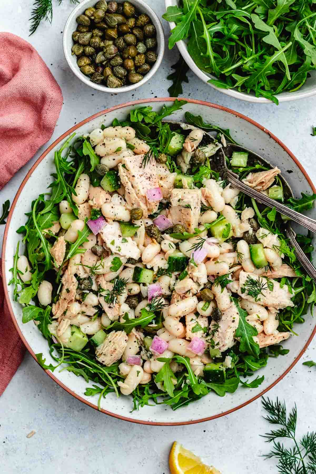 tuna white bean salad over arugula in bowl with serving spoons.