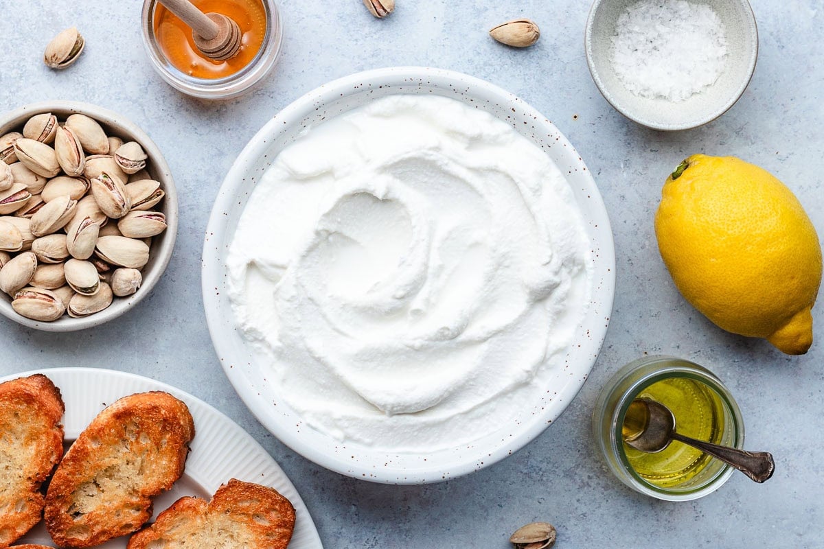 whipped ricotta in bowl with pistachios, honey, sea salt, lemon, olive oil, and crostini on the side.