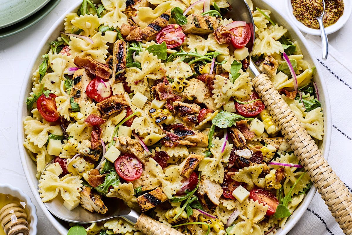close up of honey mustard chicken pasta salad in serving bowl with serving utensils.