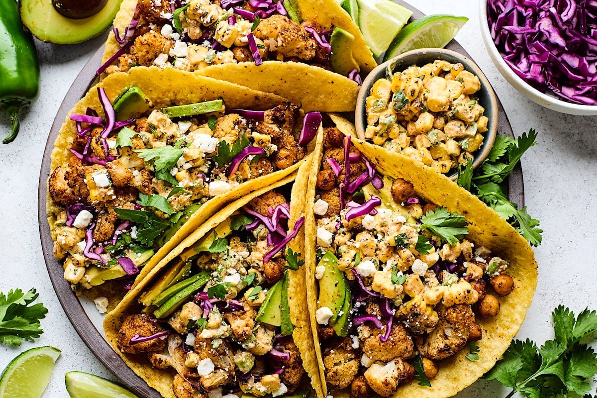 Roasted cauliflower street corn tacos on plate with toppings.