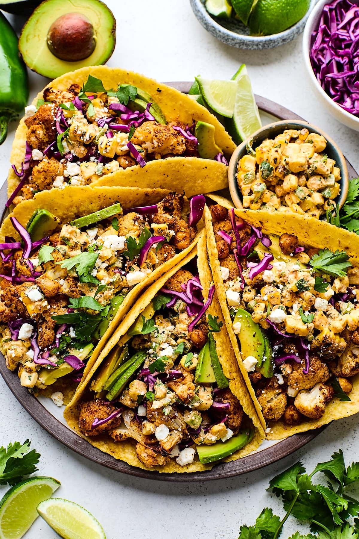 roasted cauliflower street corn tacos on plate with avocado, cilantro, cabbage, and cotija cheese.