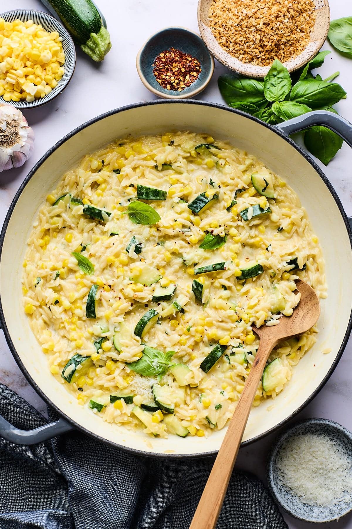 creamy corn and zucchini orzo in skillet with wooden spoon.