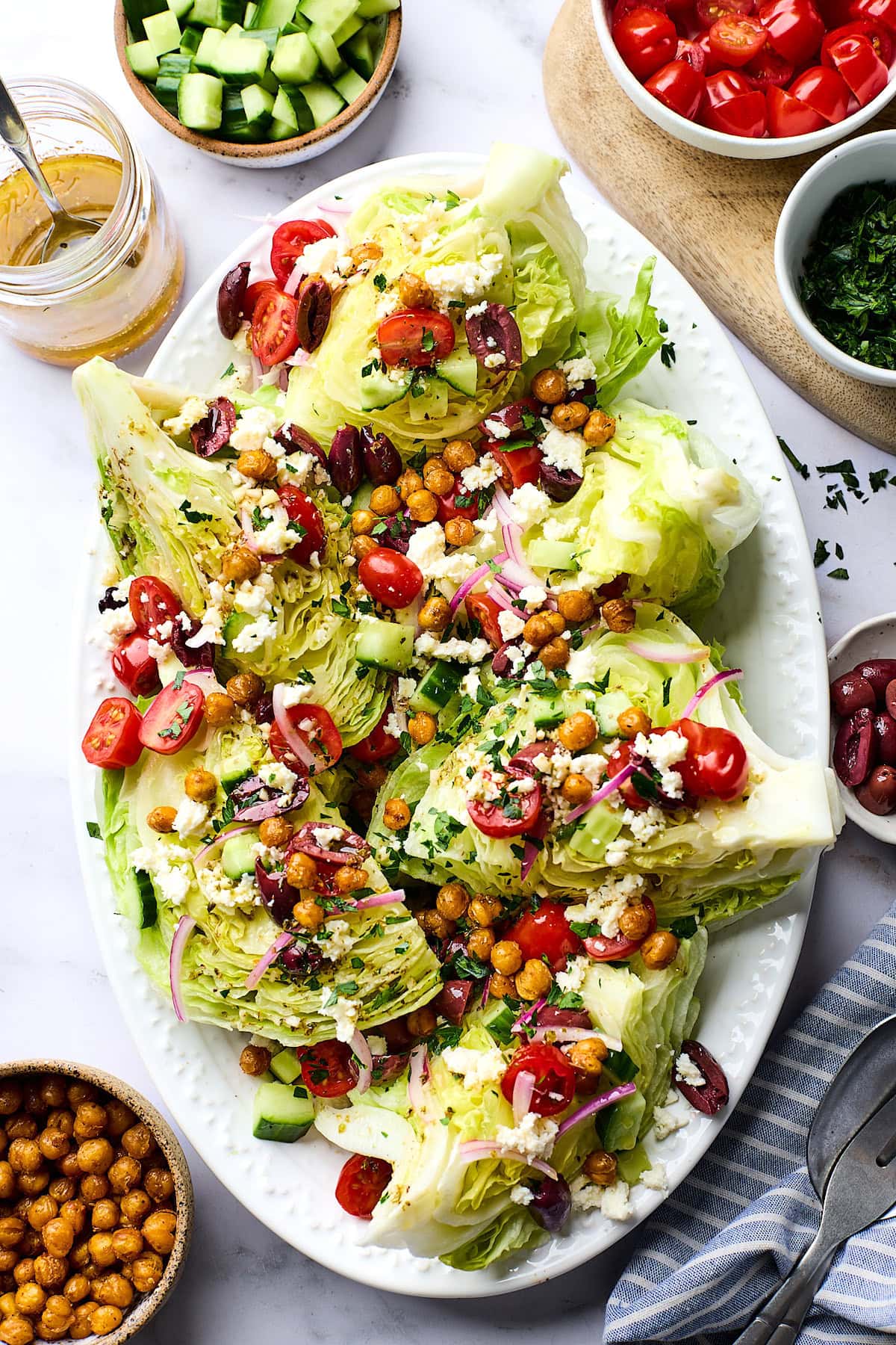 Greek wedge salad with crispy chickpeas, tomatoes, cucubmer, red onion, olives, herbs, and feta on platter.