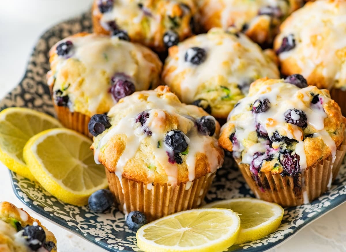 lemon blueberry zucchini muffins with lemon glaze on plate with lemon slices.