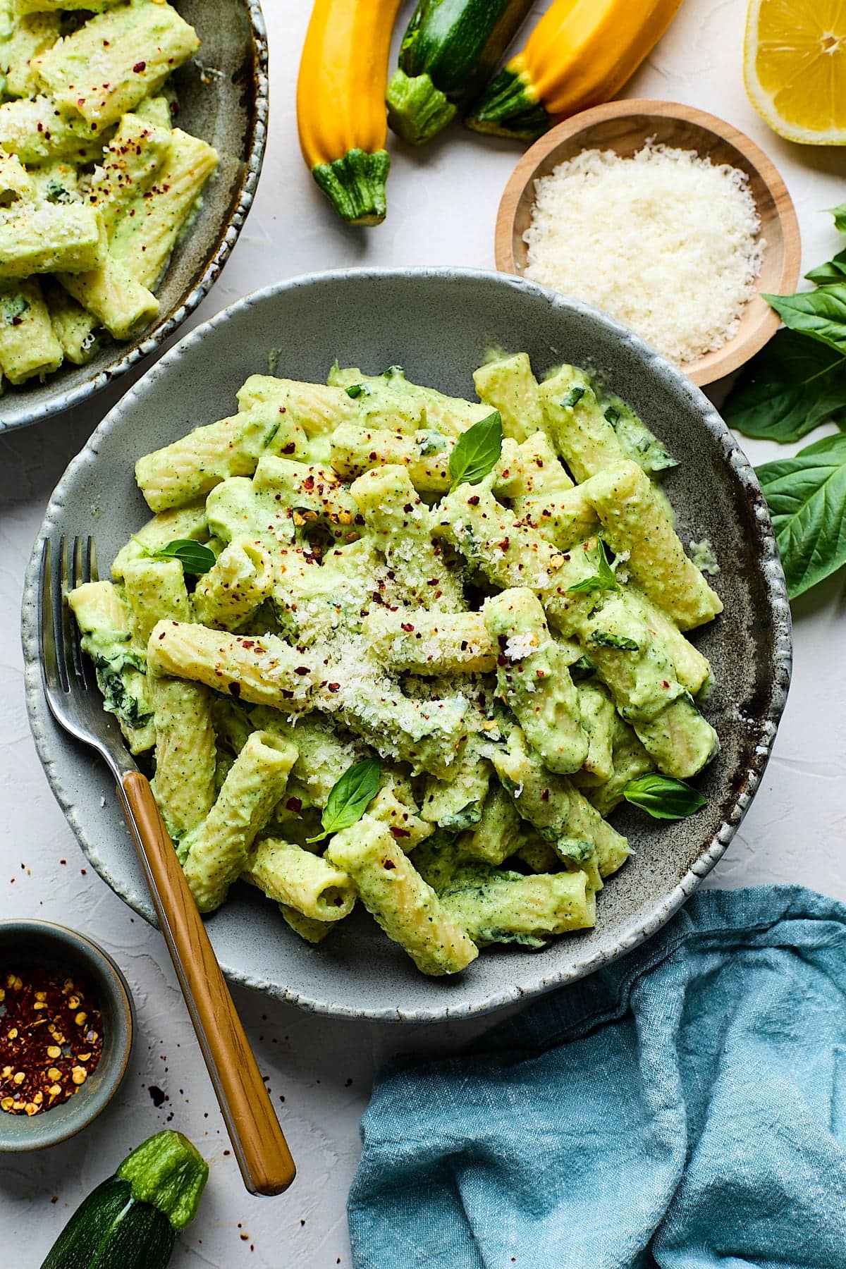 zucchini pasta in bowl with basil, parmesan cheese, crushed red pepper flakes and fork.