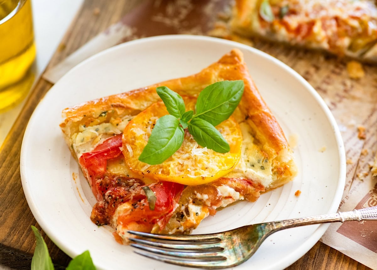 slice of tomato tart with basil on plate with fork.