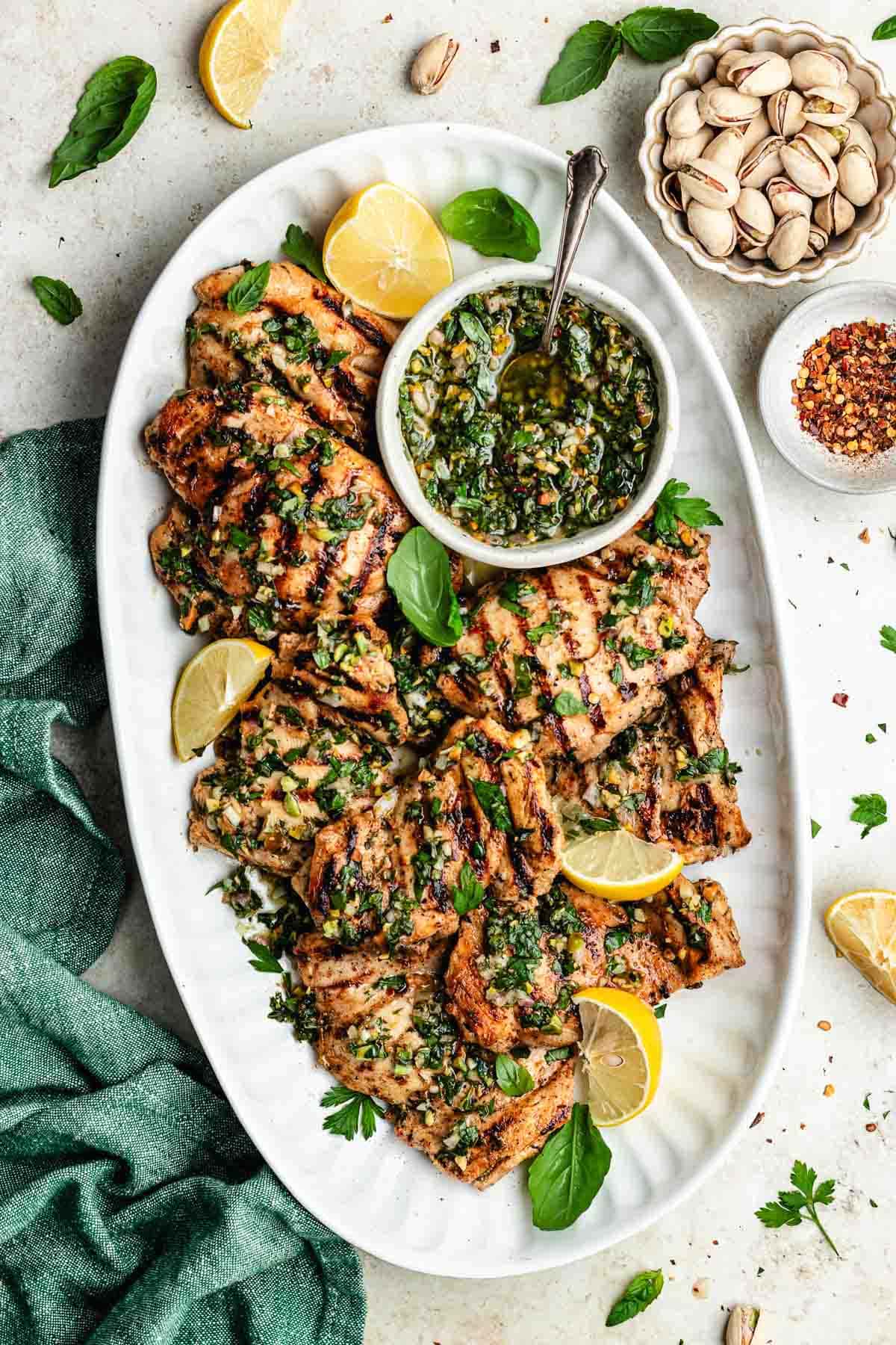 grilled lemon herb chicken thighs with pistachio chimichurri on platter.