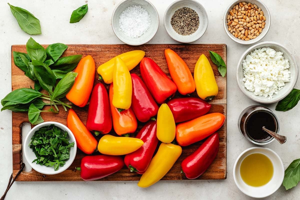 mini sweet peppers and basil on wood board and ingredients in bowl to make grilled mini sweet peppers.