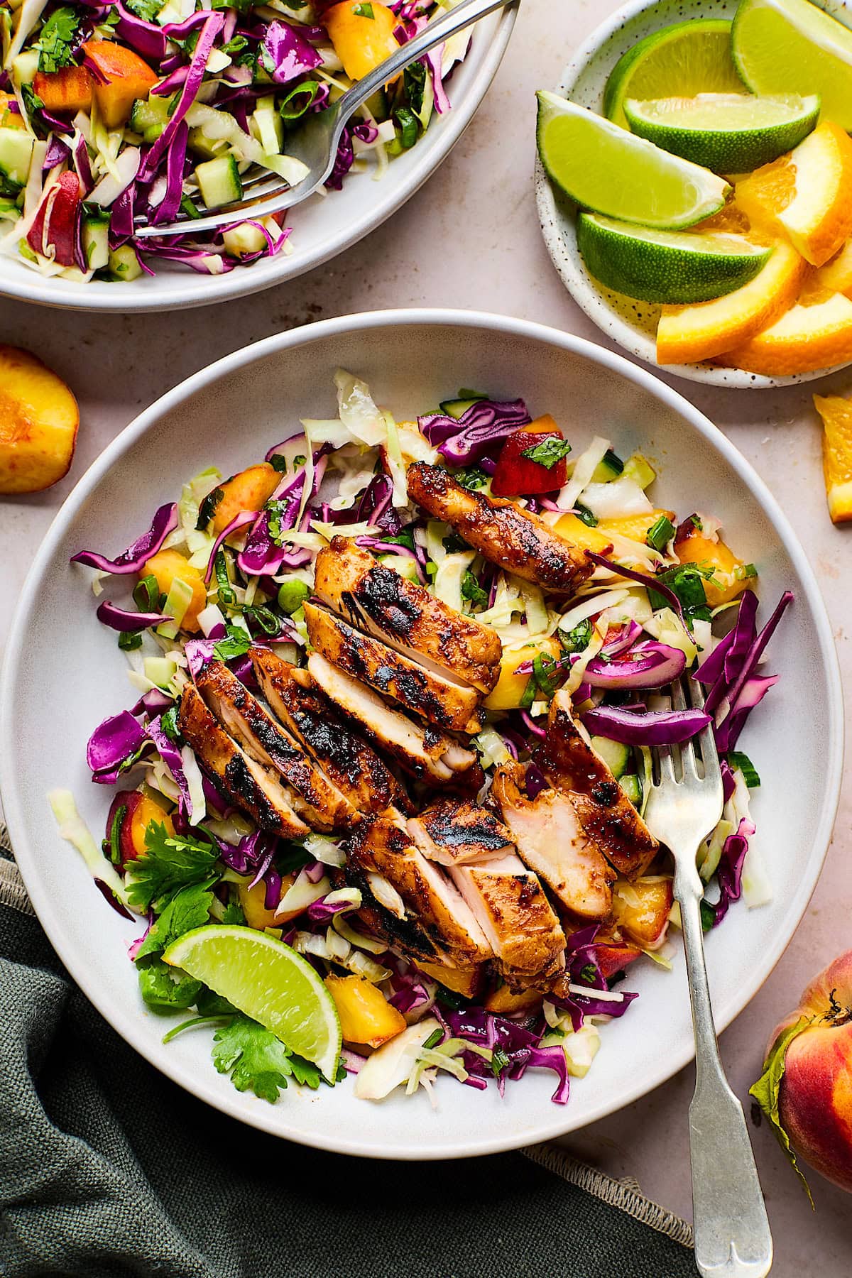 honey chipotle chicken thighs sliced over peach slaw in bowl with fork.