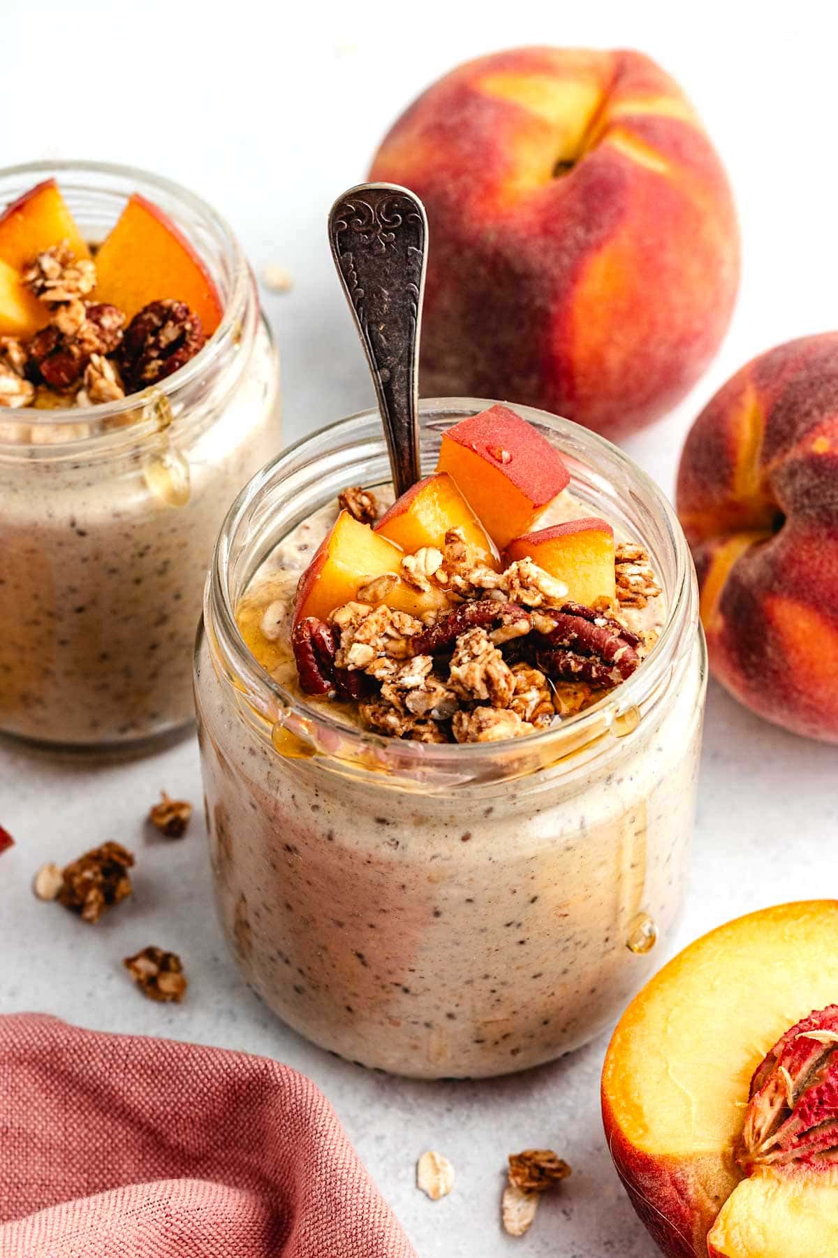 peach overnight oats in jar with granola, fresh peaches, and spoon.