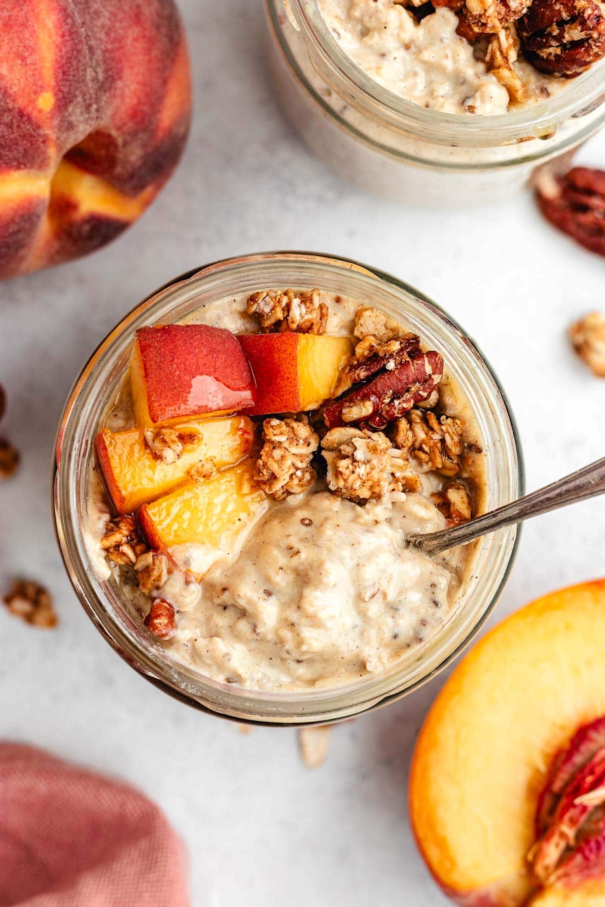 close up of peach overnight oats in jar with spoon and toppings.
