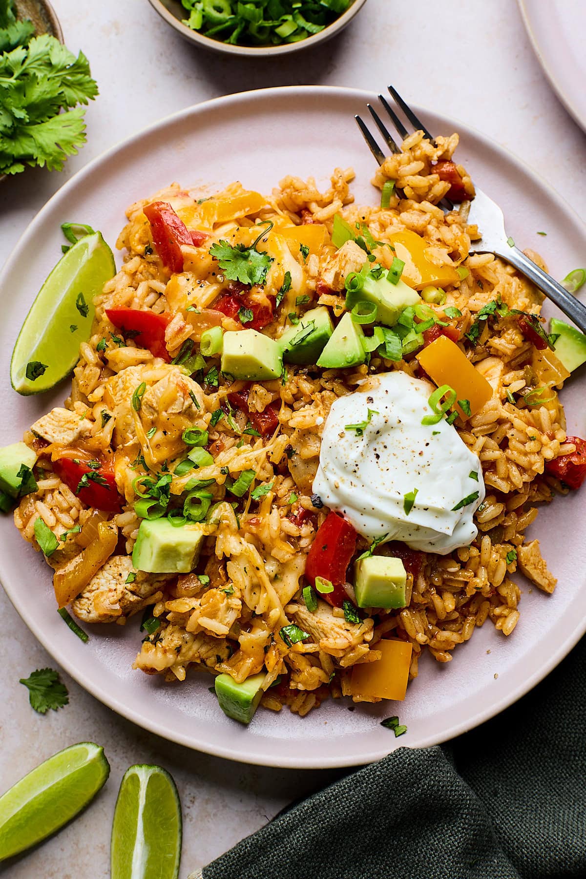 chicken fajita skillet on plate with sour cream, avocado, green onion, lime wedge, and fork.