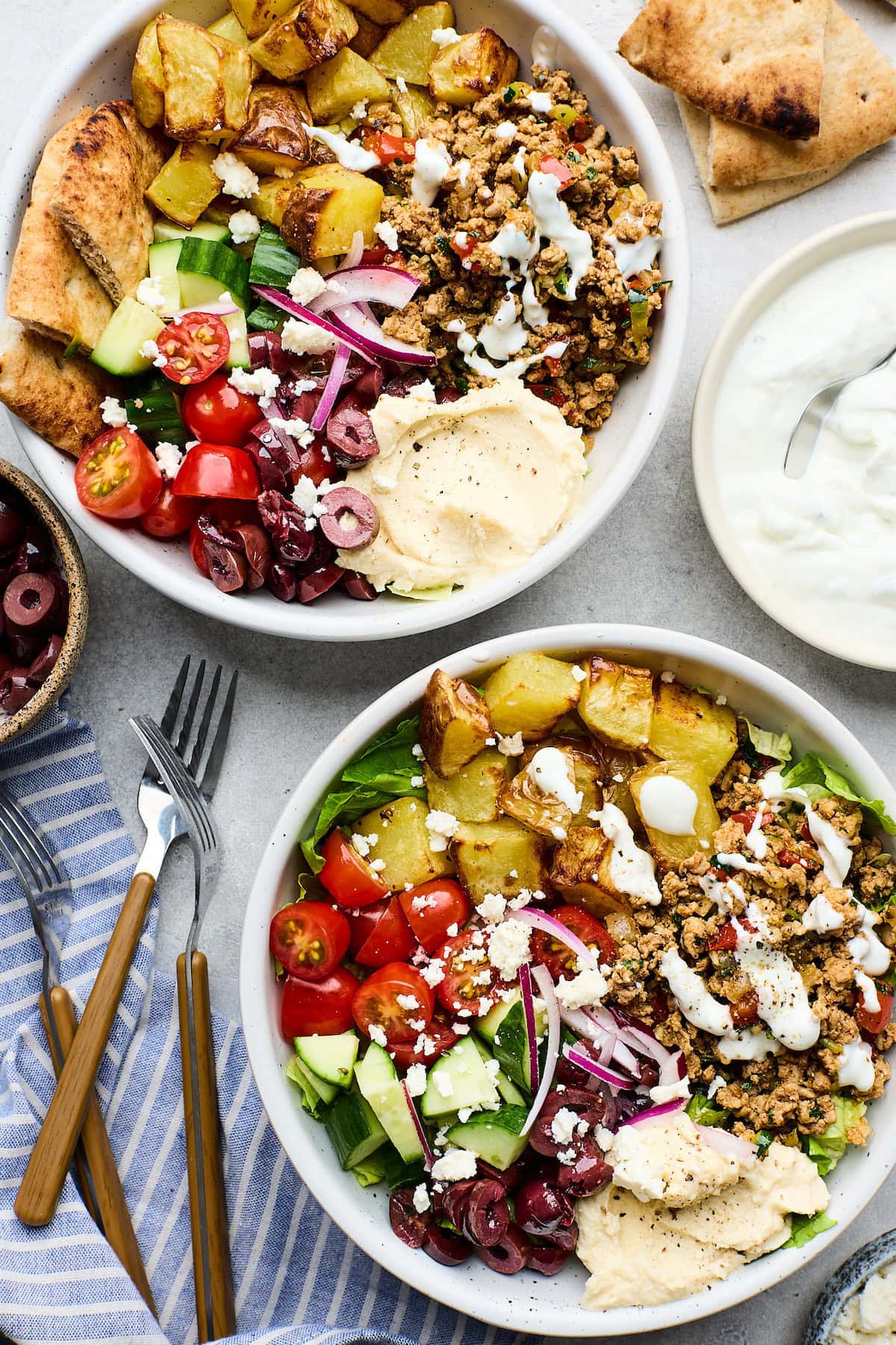 Greek ground turkey bowls with potatoes, tomatoes, cucumber, olives, red onion, hummus, and tzatziki.
