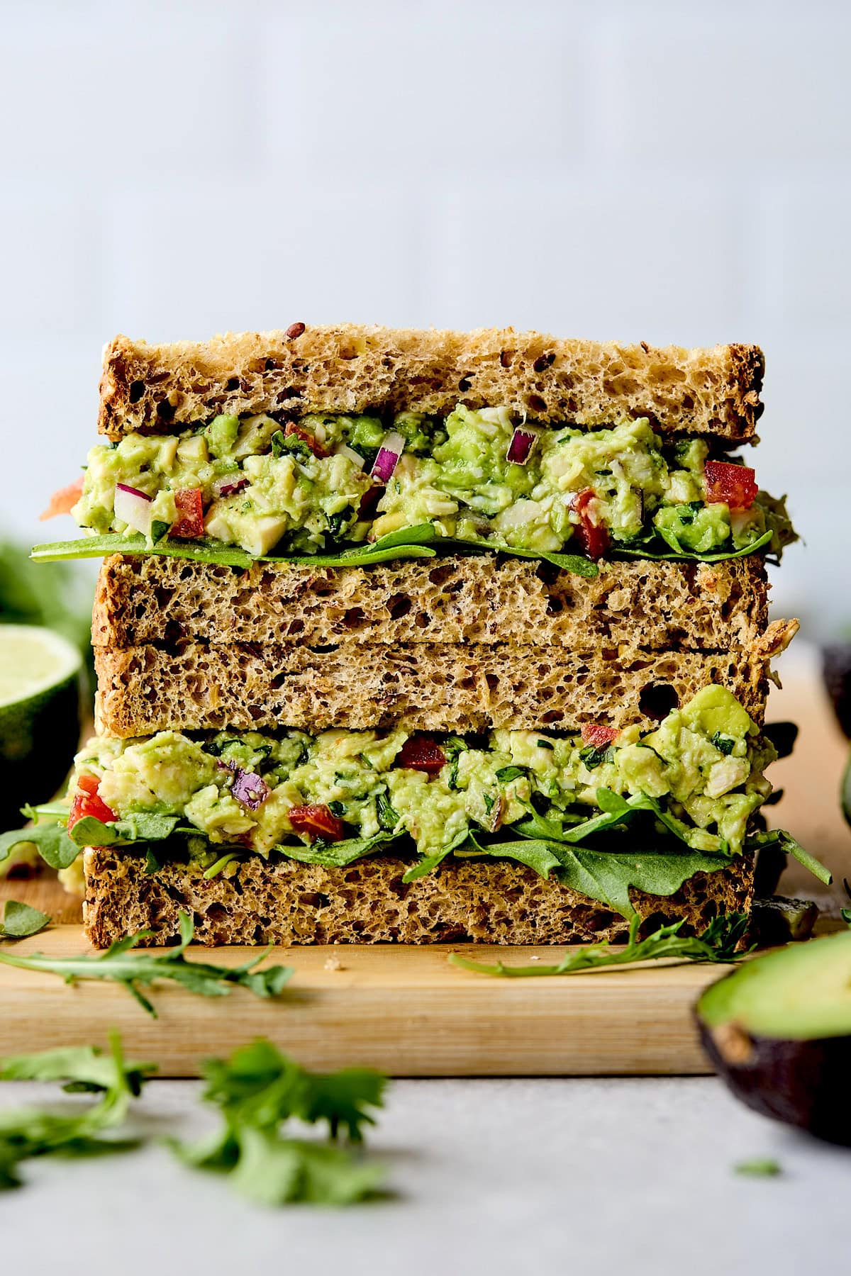 guacamole chicken salad sandwich stacked on wood cutting board.