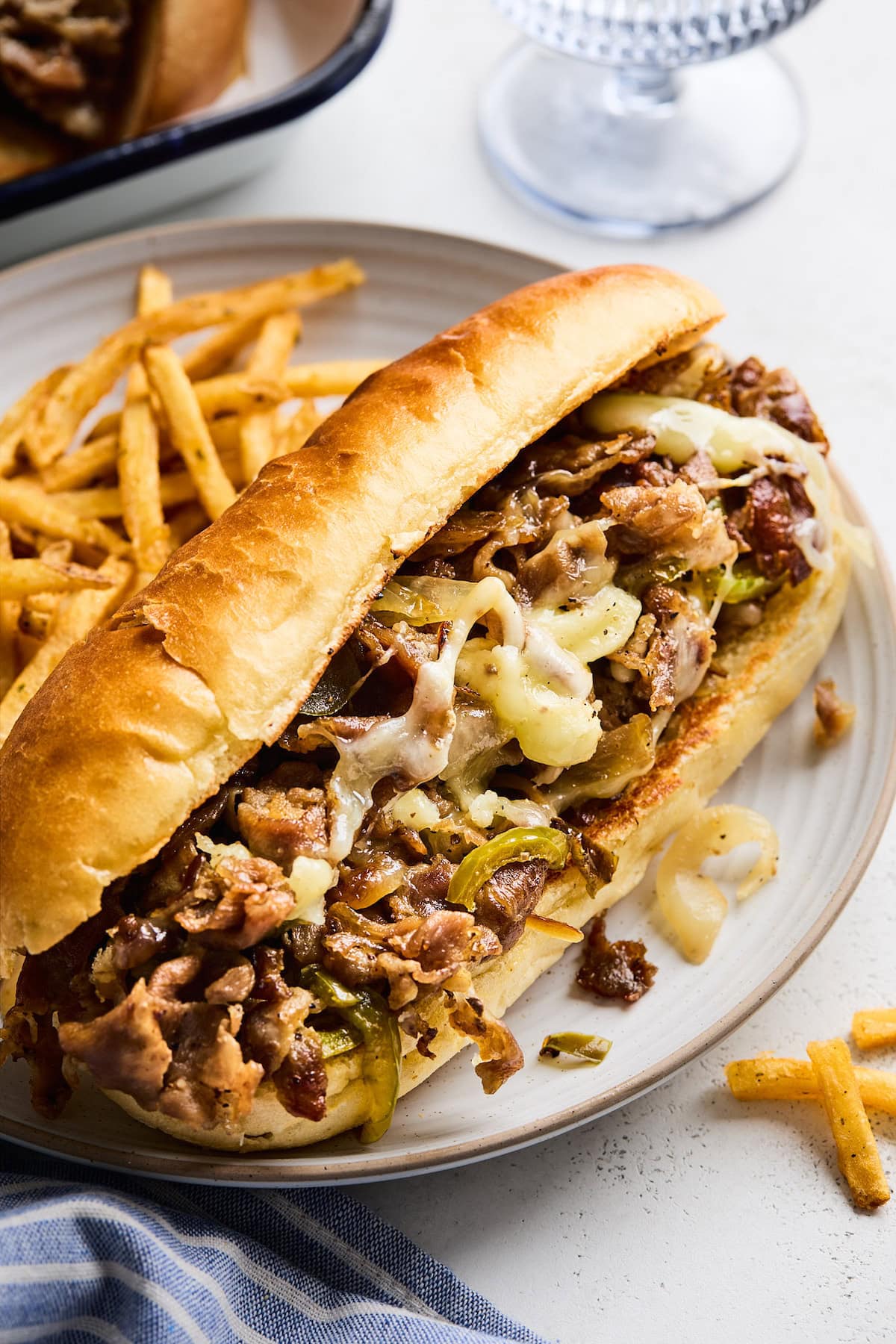 Philly cheesesteak on hoagie roll on plate with french fries.