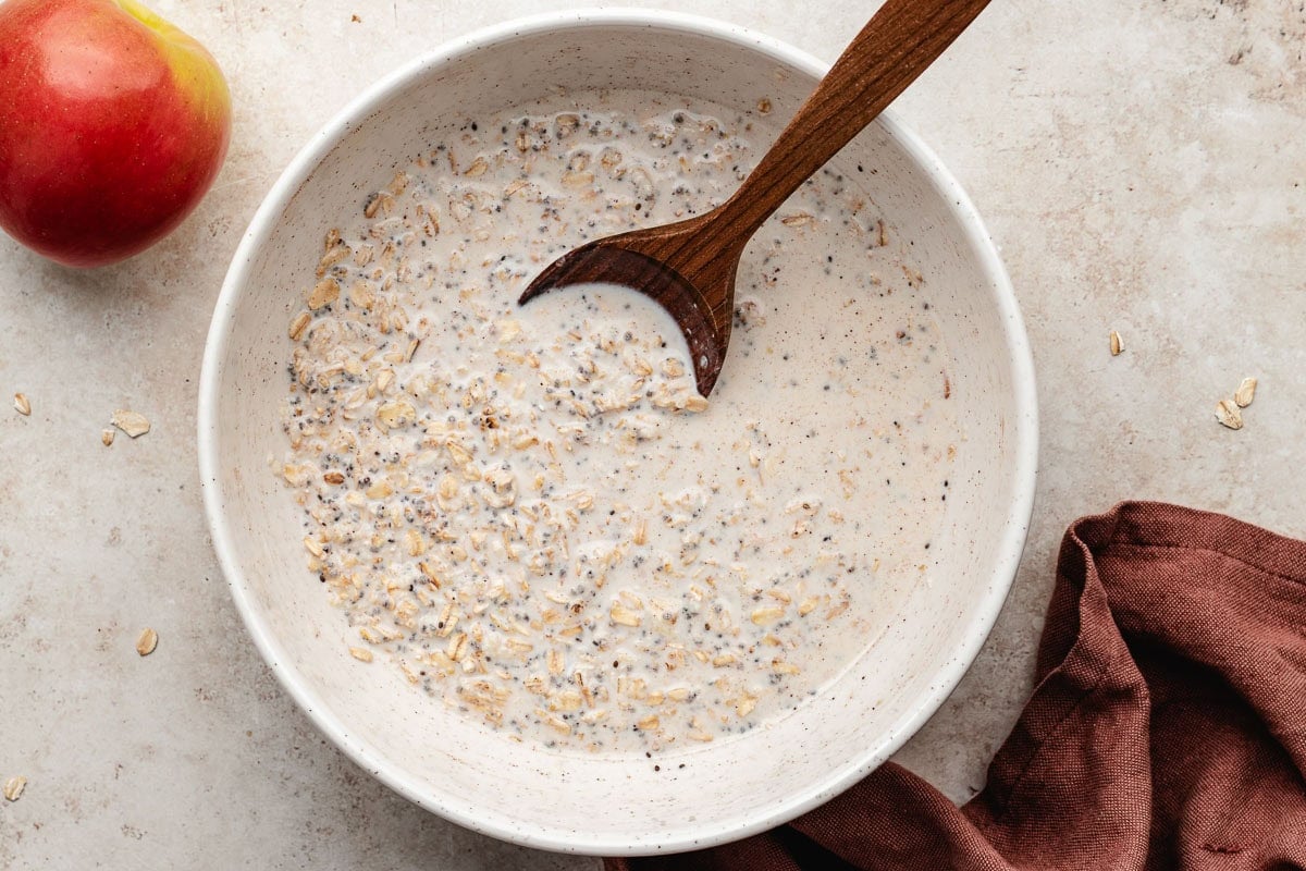 overnight oat mixture being stirred together with wooden spoon in white bowl.