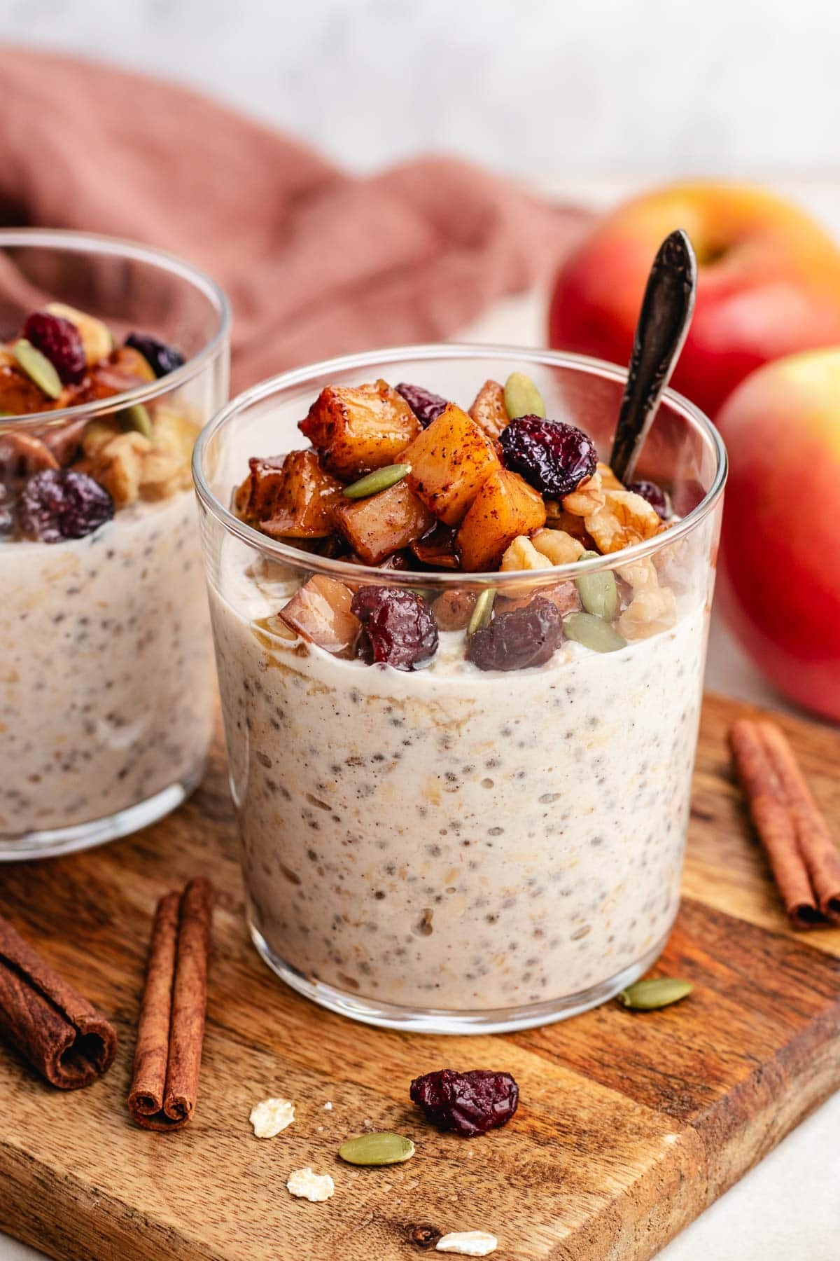 apple pie overnight oats in glass jars with cinnamon apples, dried cranberries, and nuts.