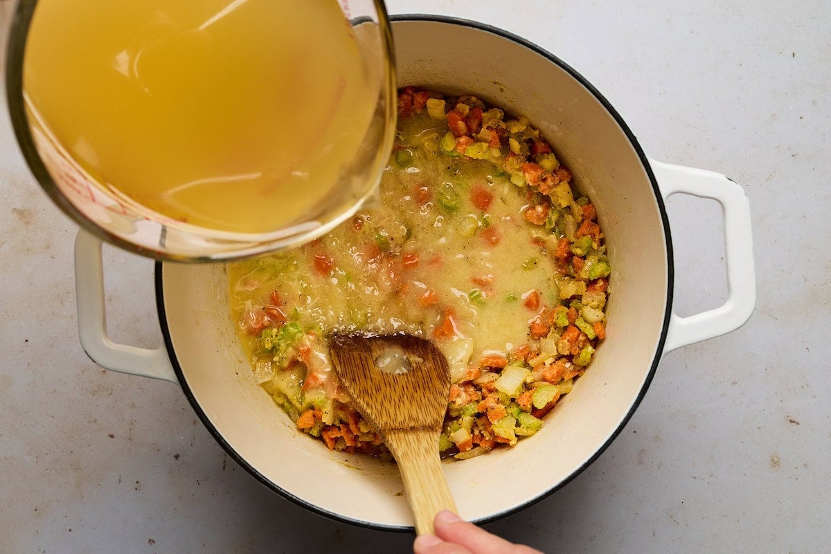 broth being poured into vegetable roux to make cheeseburger soup.